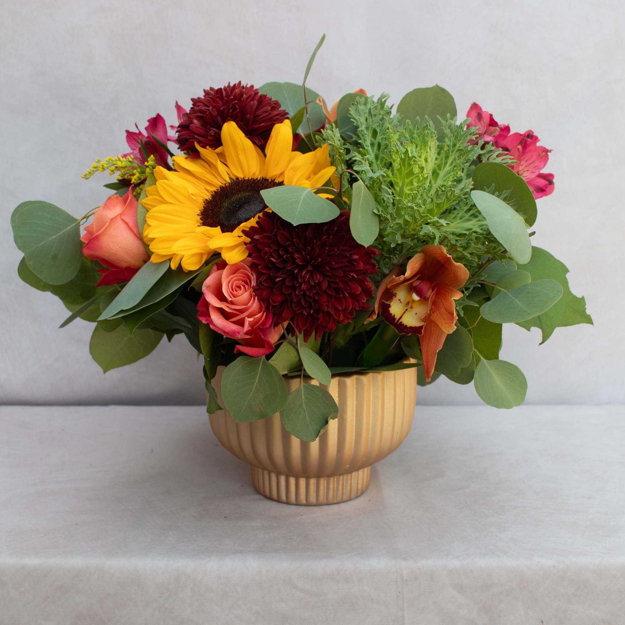 Mixed bouquet with sunflowers, roses, and mums in a gold vase