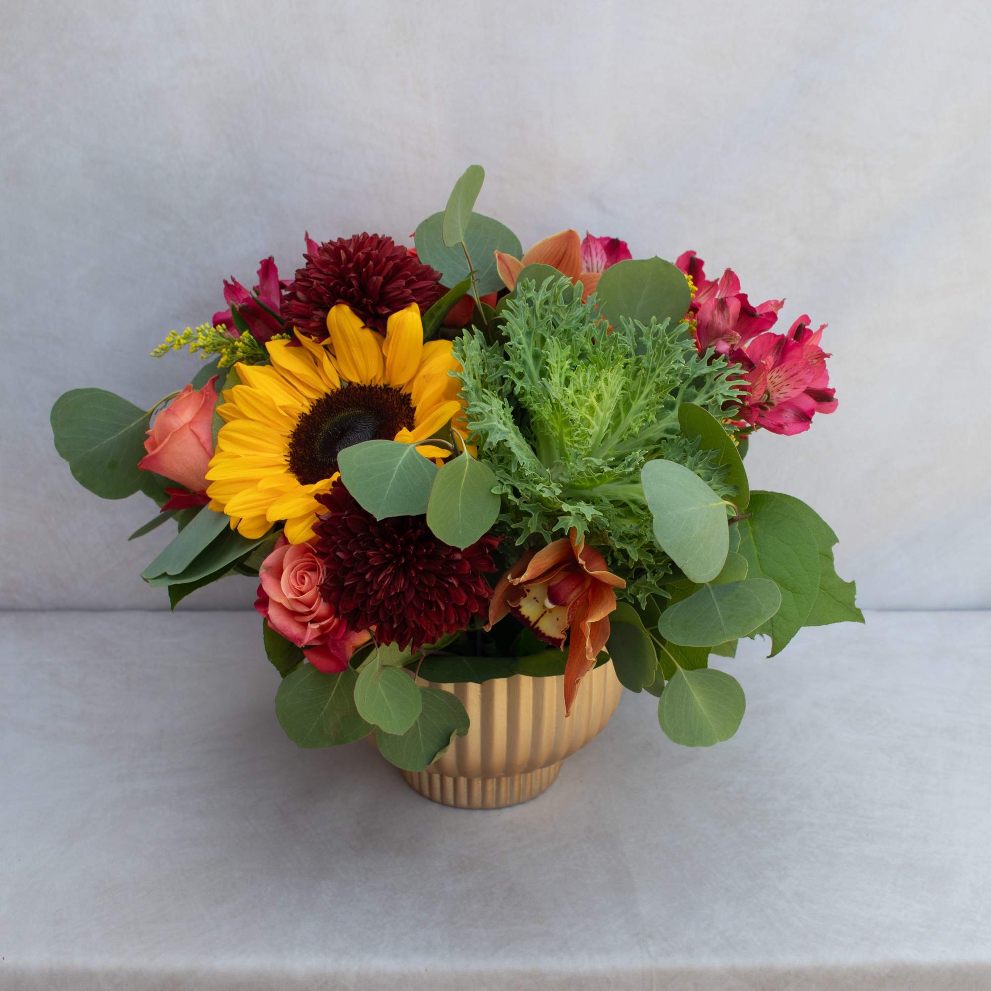Mixed bouquet with a sunflower, roses, and pink blooms in a gold vase