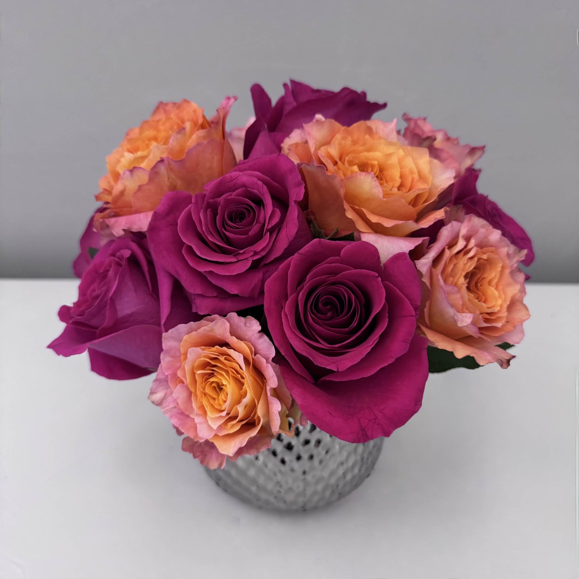 Bouquet of magenta and peach roses in a textured silver vase