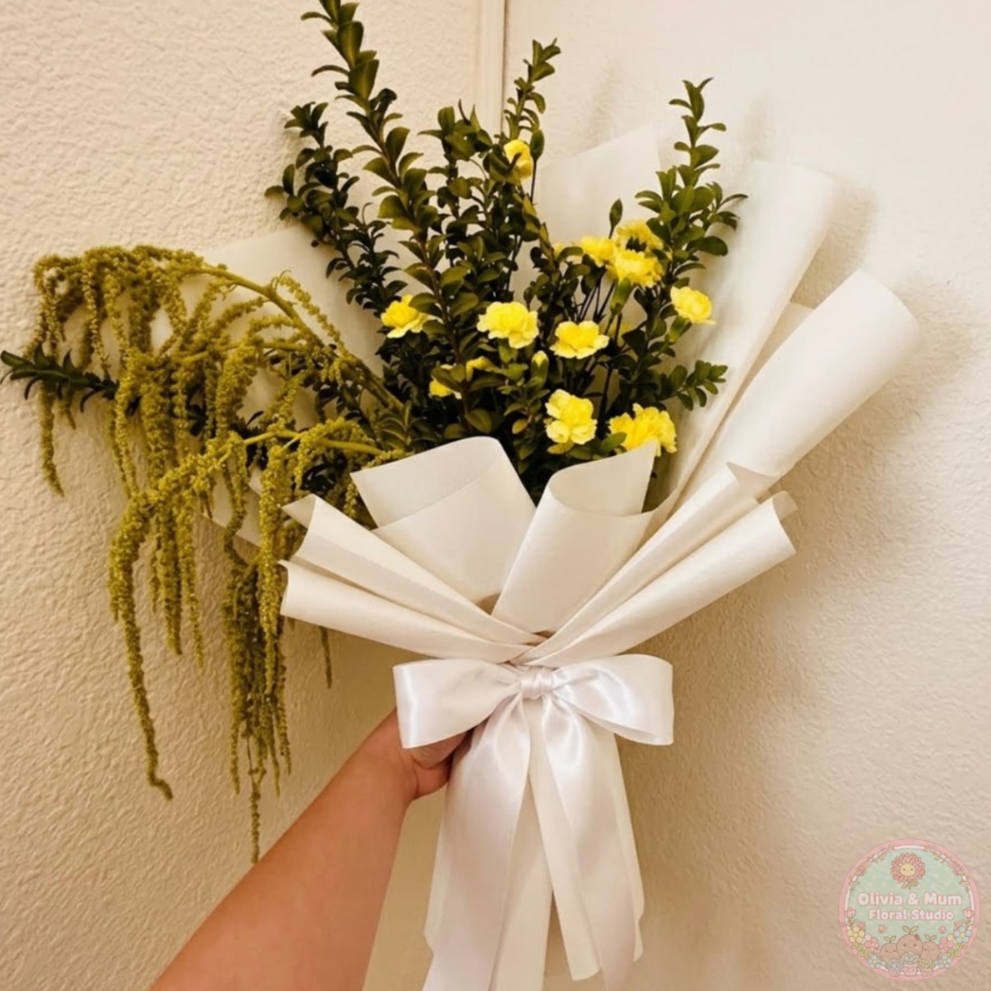 Handheld bouquet with yellow flowers, greenery, and white wrapping tied with a satin bow