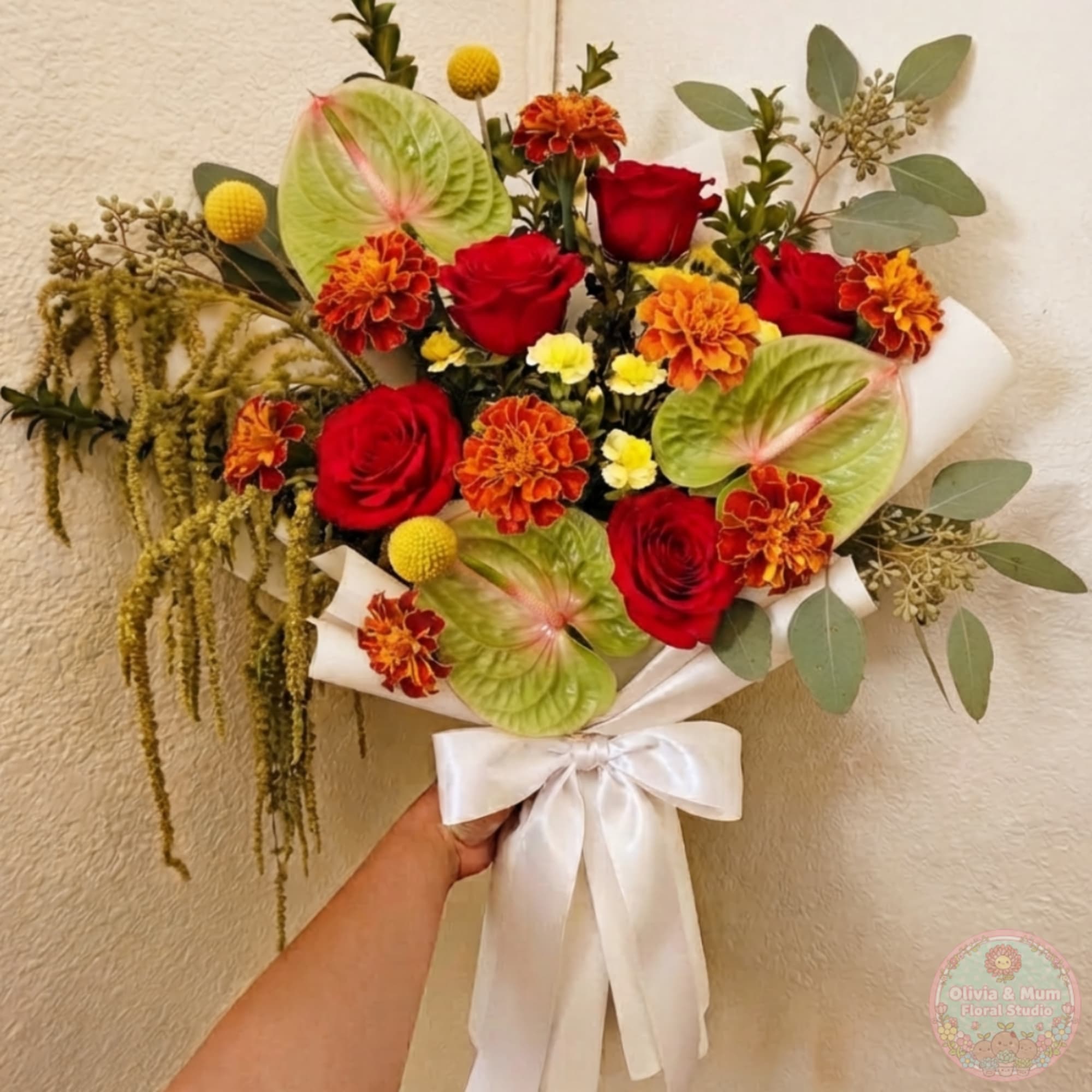 Handheld bouquet of red roses, orange flowers, and green anthuriums with a white ribbon