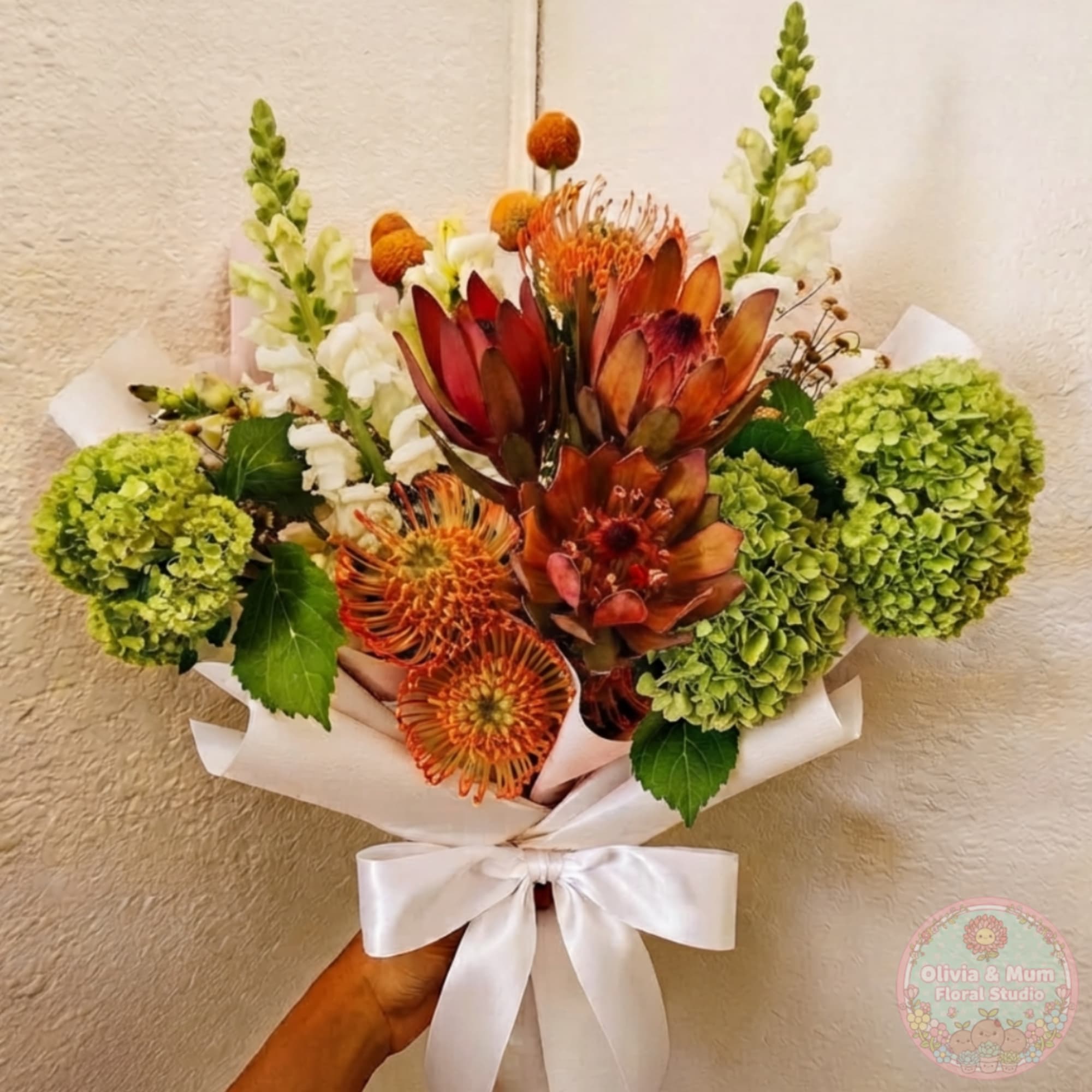Bouquet with orange protea, green hydrangeas, and white snapdragons wrapped in white paper