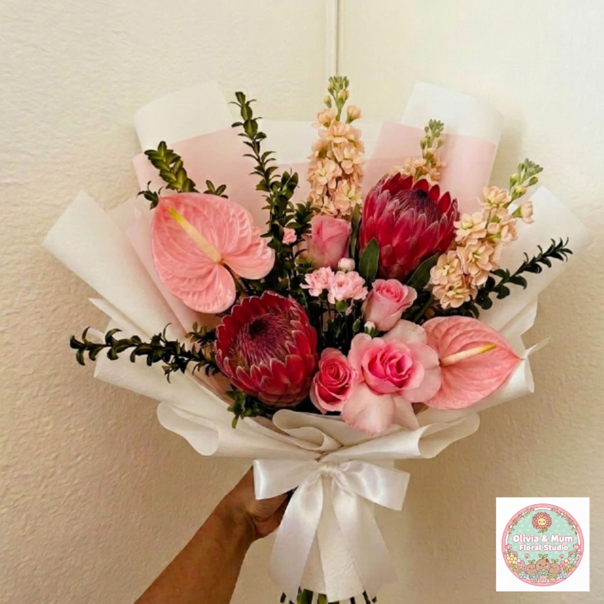 Pink and red mixed bouquet with protea, roses, and anthuriums wrapped in white paper