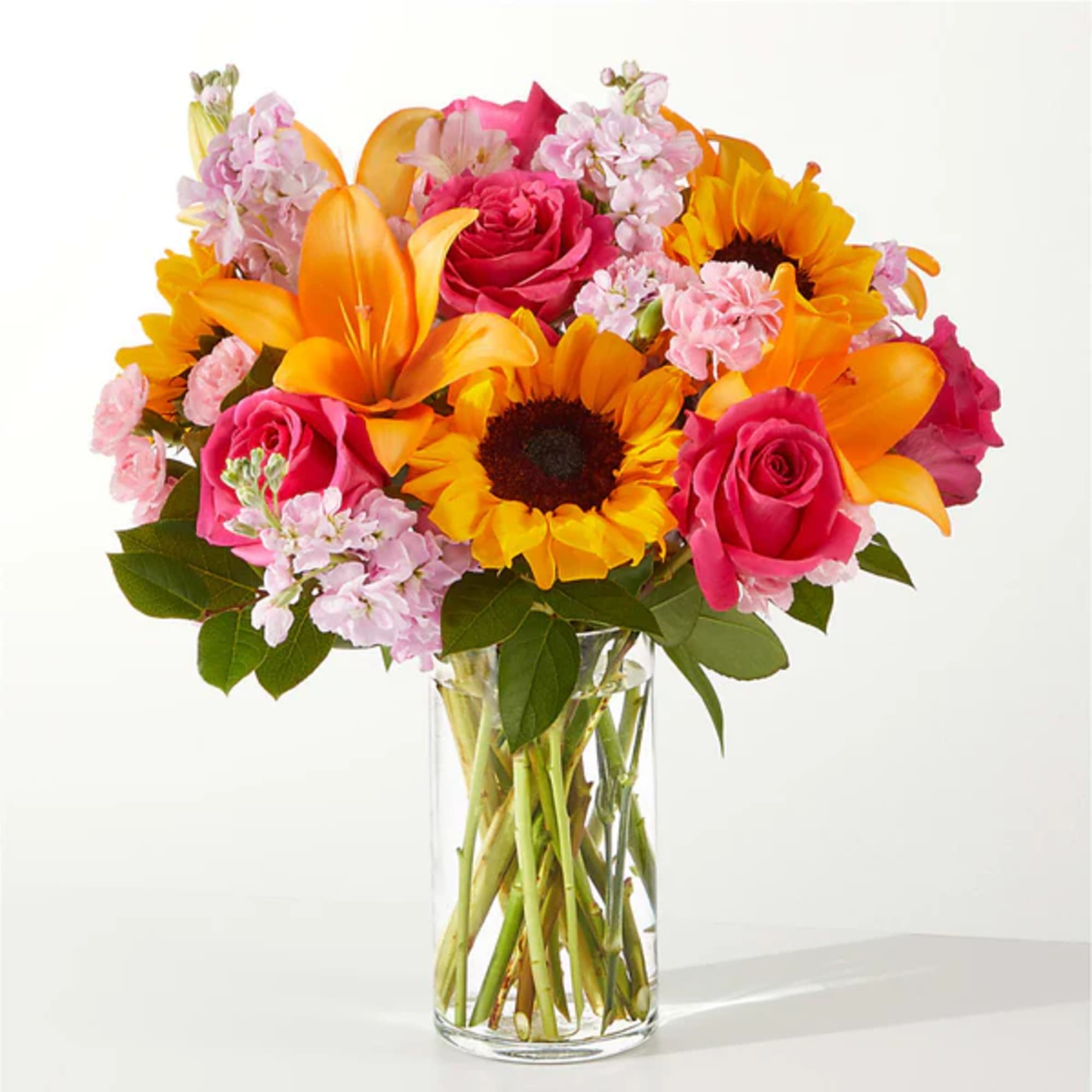 Bouquet of pink roses, sunflowers, and orange lilies in a clear glass vase