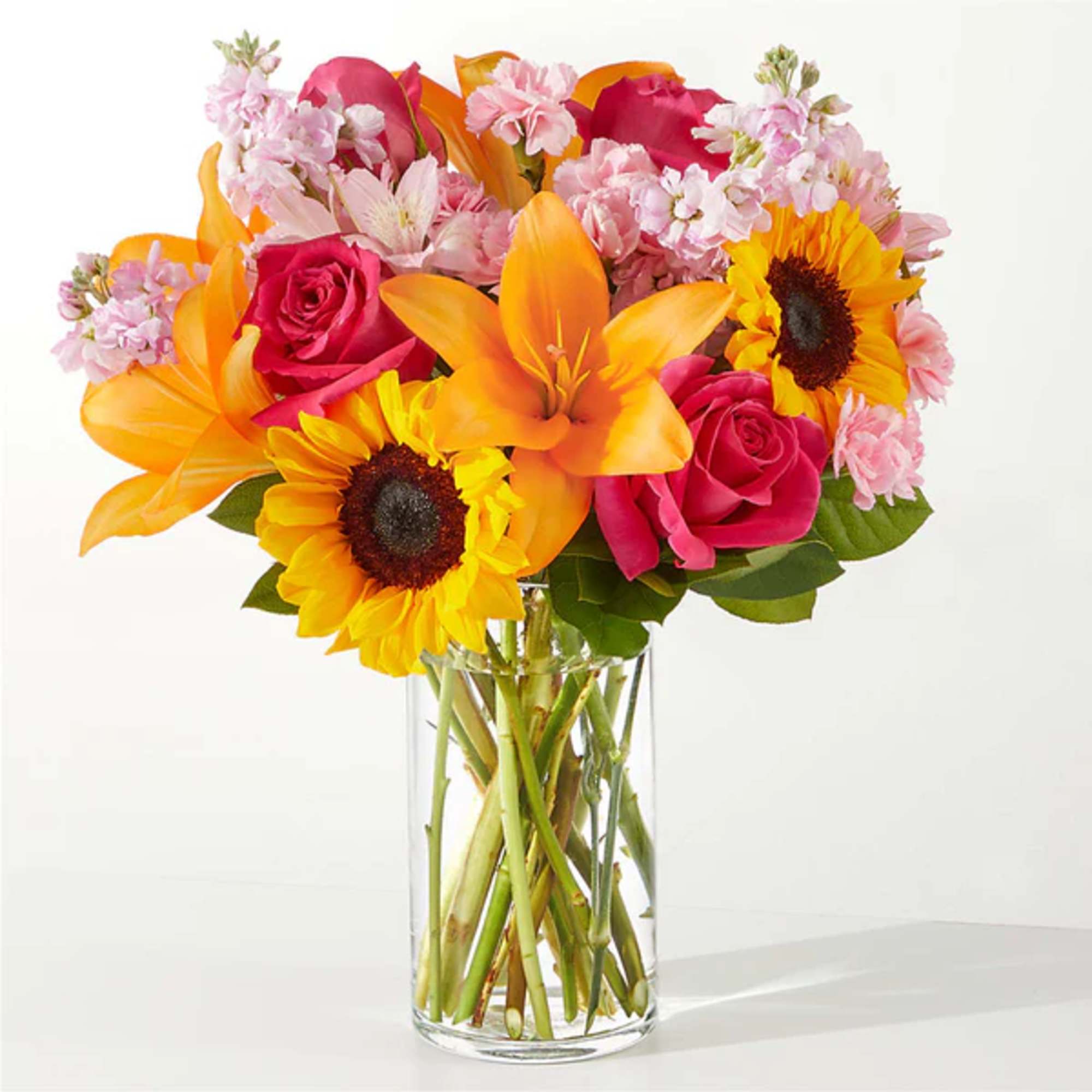 Bouquet of pink roses, orange lilies, and sunflowers in a clear glass vase