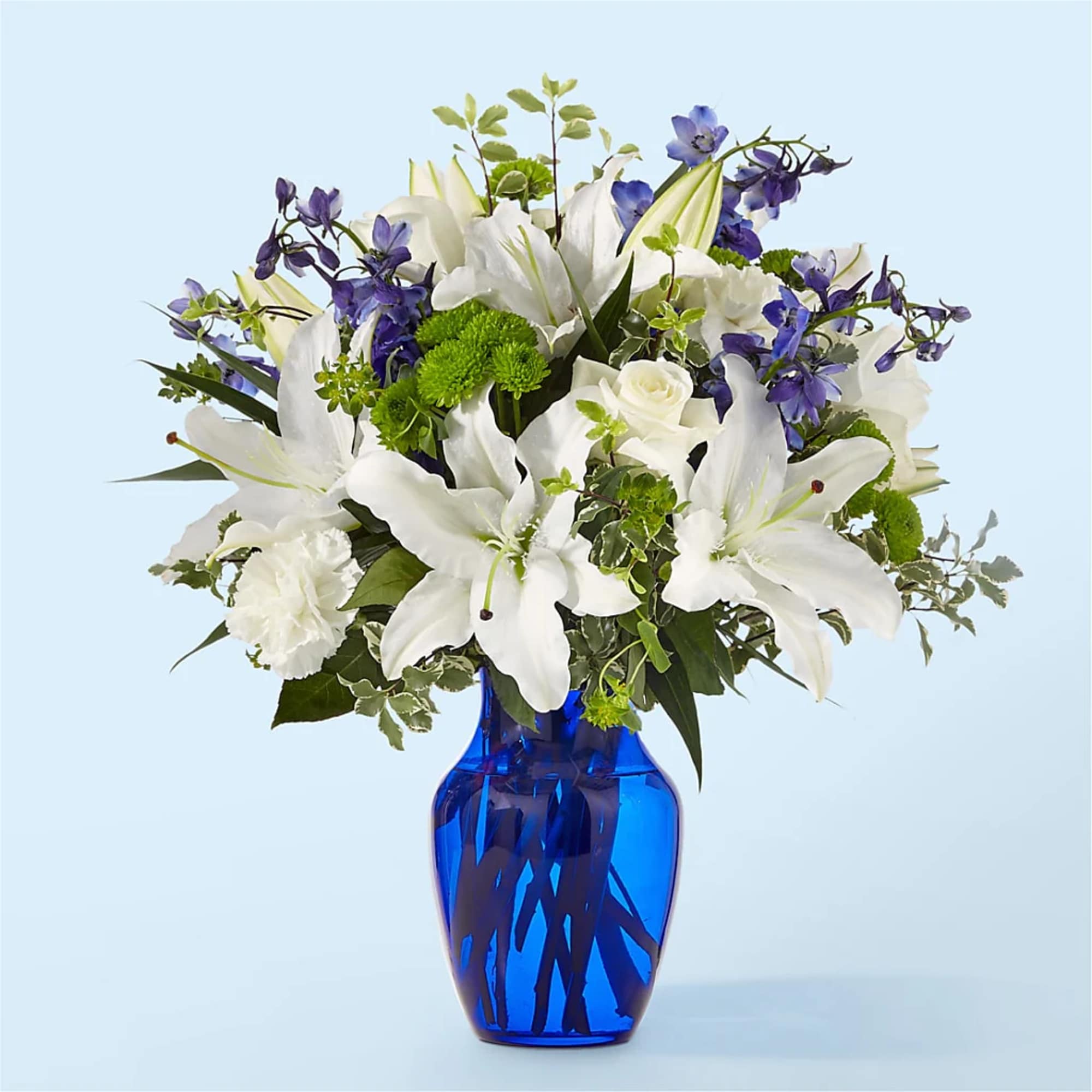 White lilies and purple flowers in a blue glass vase
