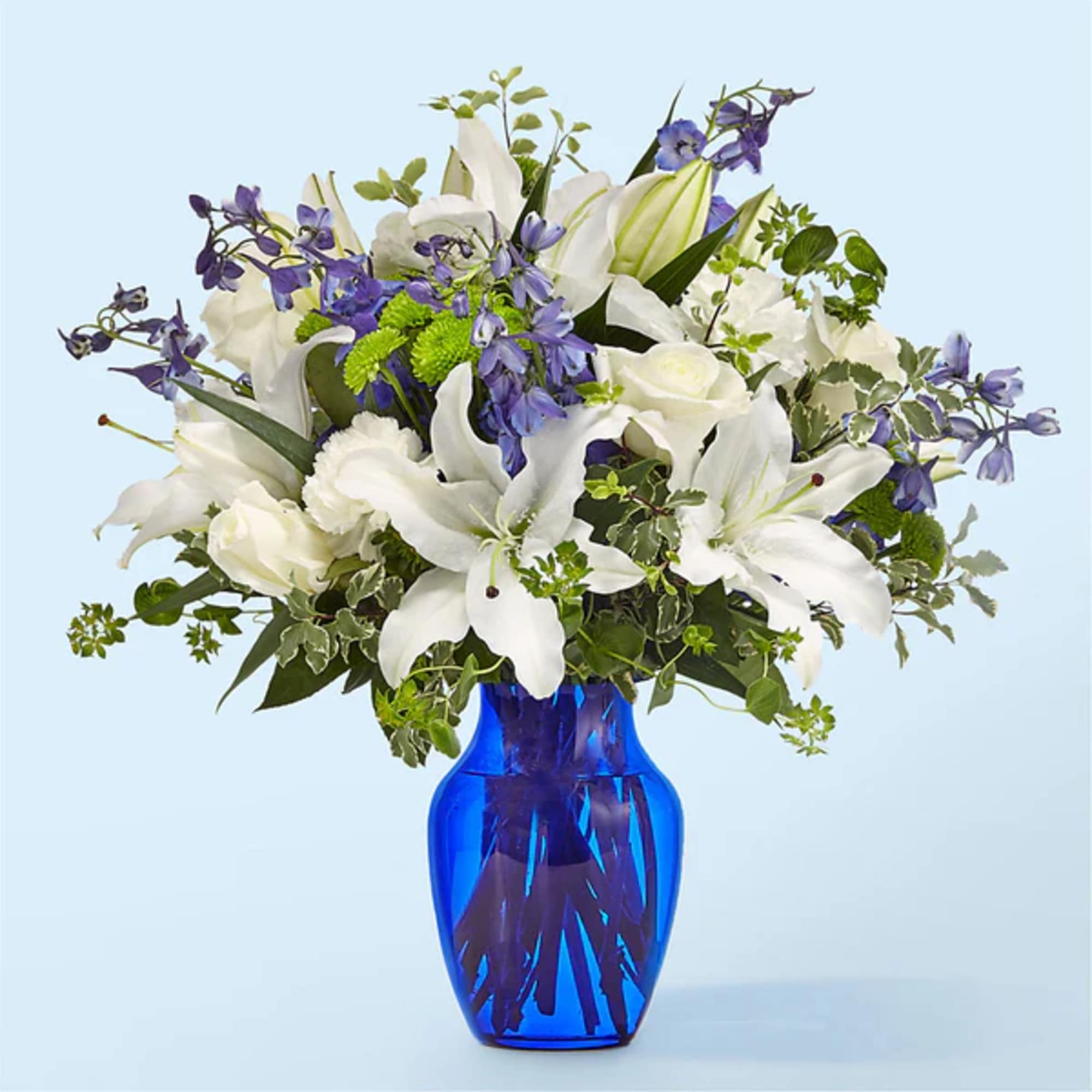 White lilies and roses with purple flowers in a blue glass vase