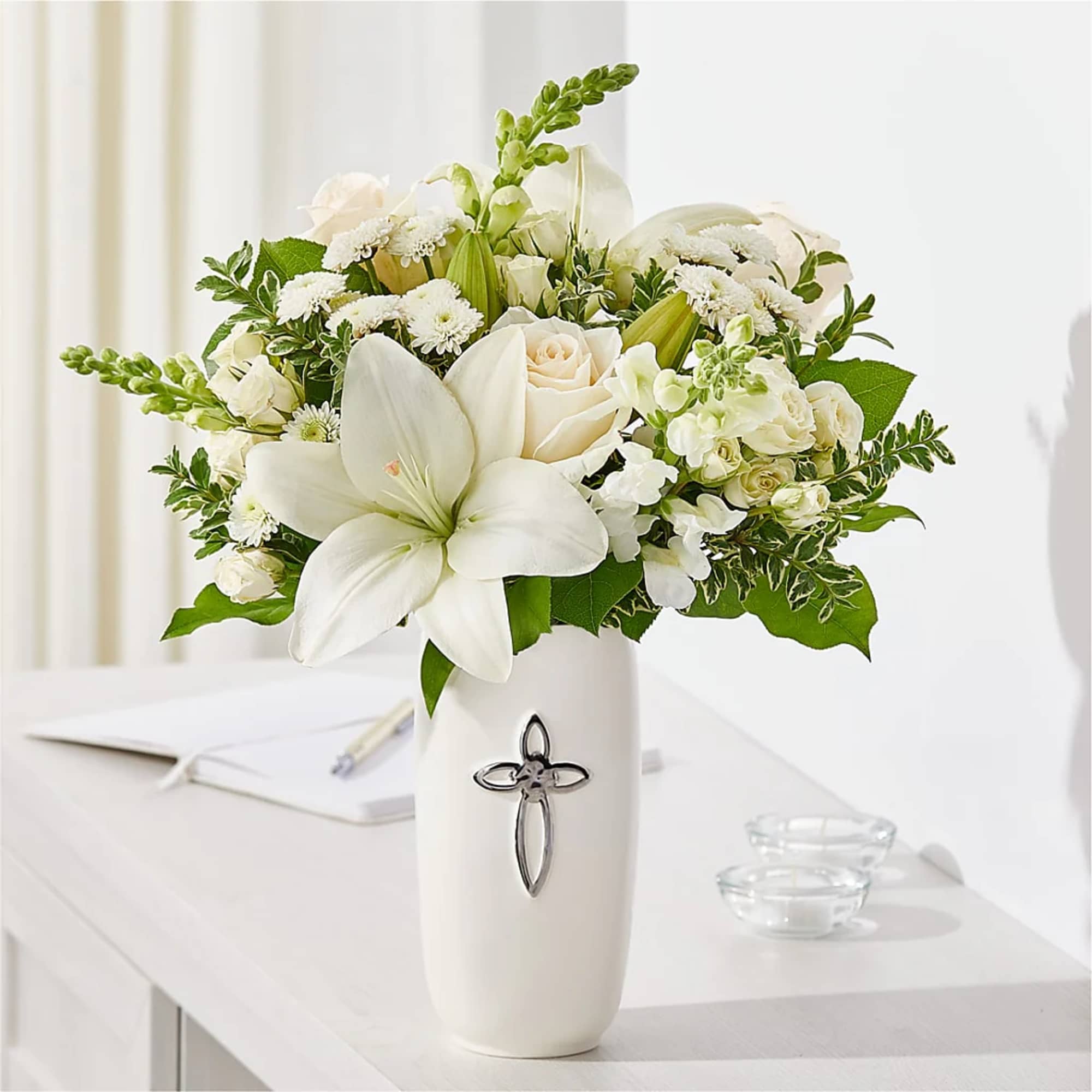White floral arrangement in a tall vase with a cross emblem