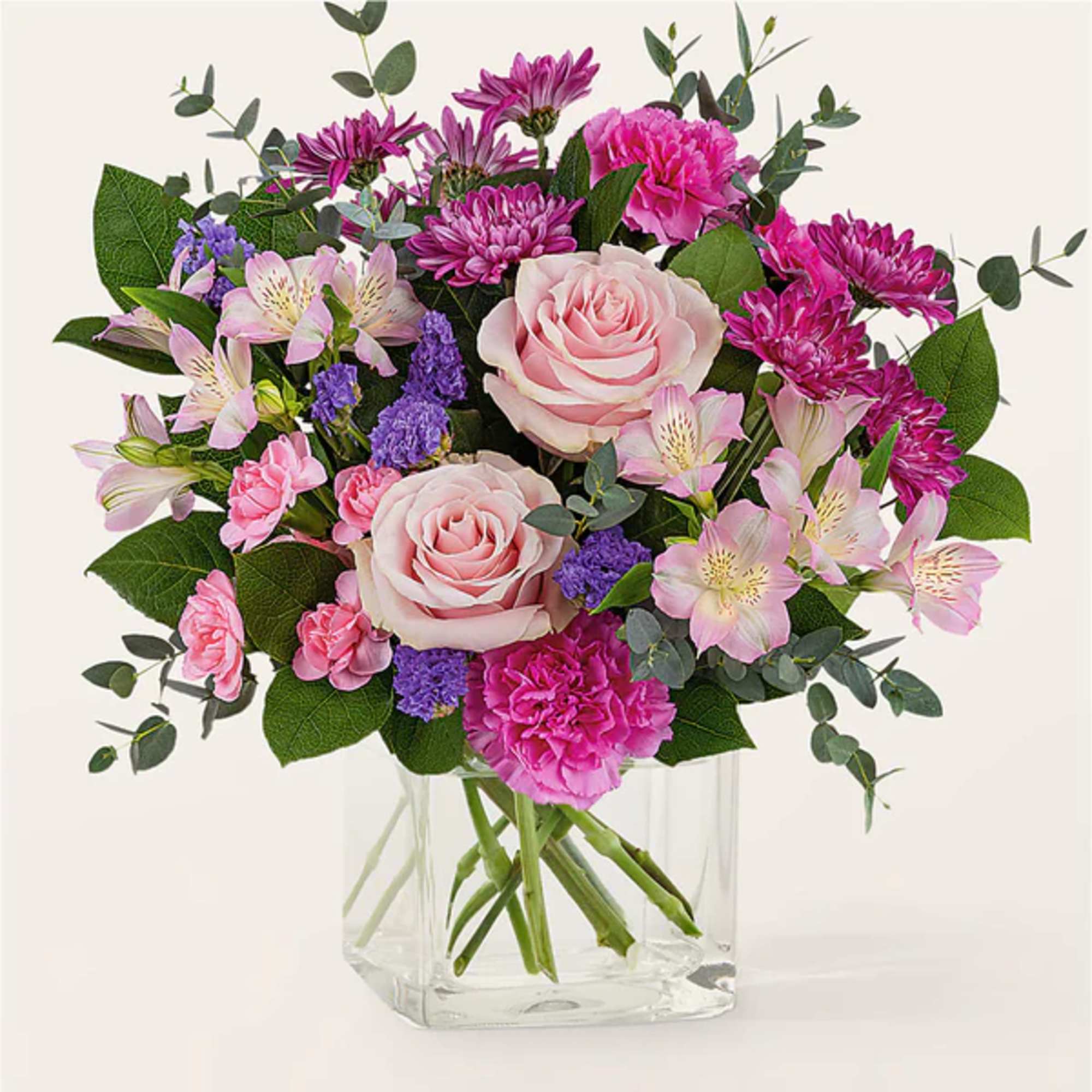 Bouquet of pink roses, carnations, and purple flowers in a clear glass vase