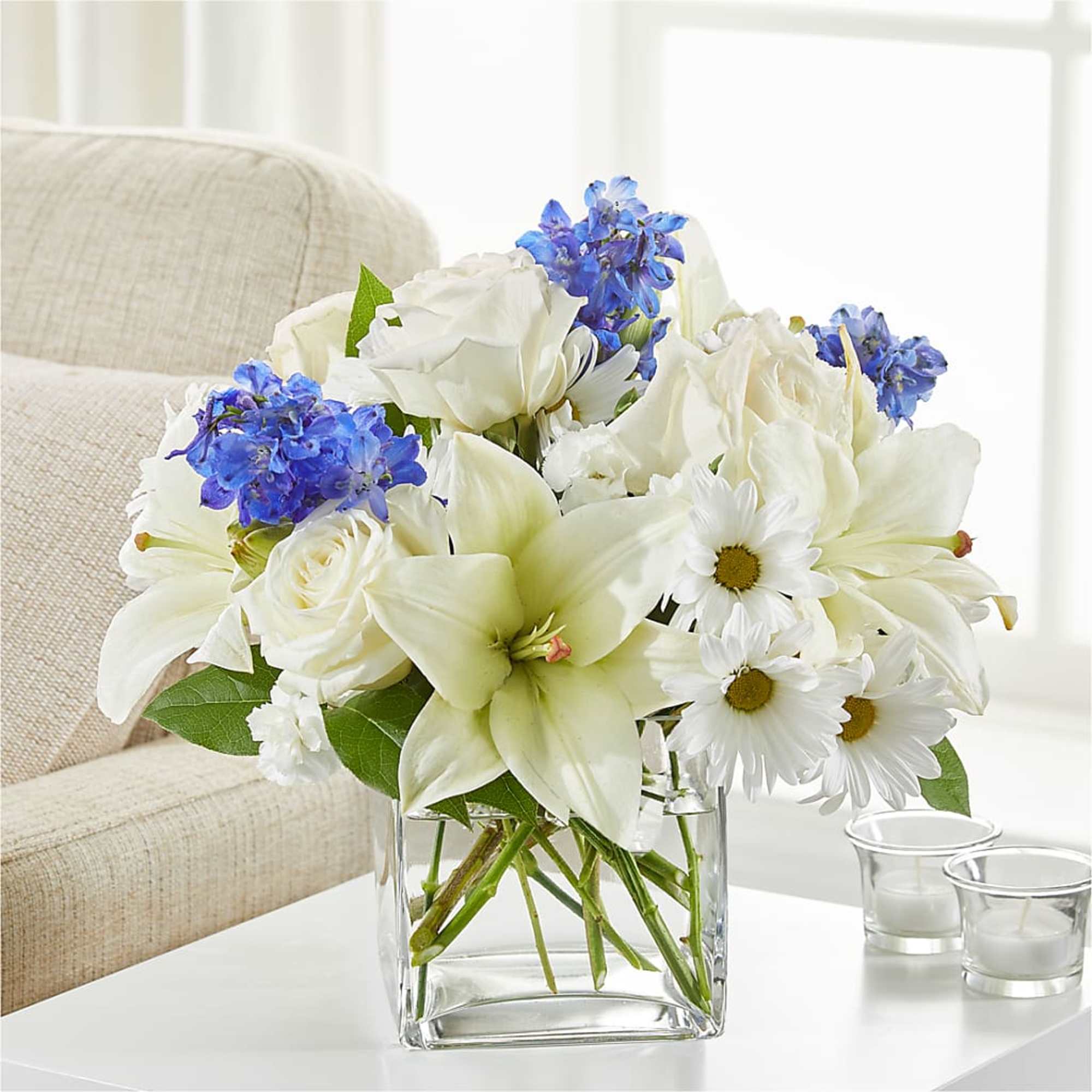 White roses, lilies, and daisies with blue flowers in a clear glass vase