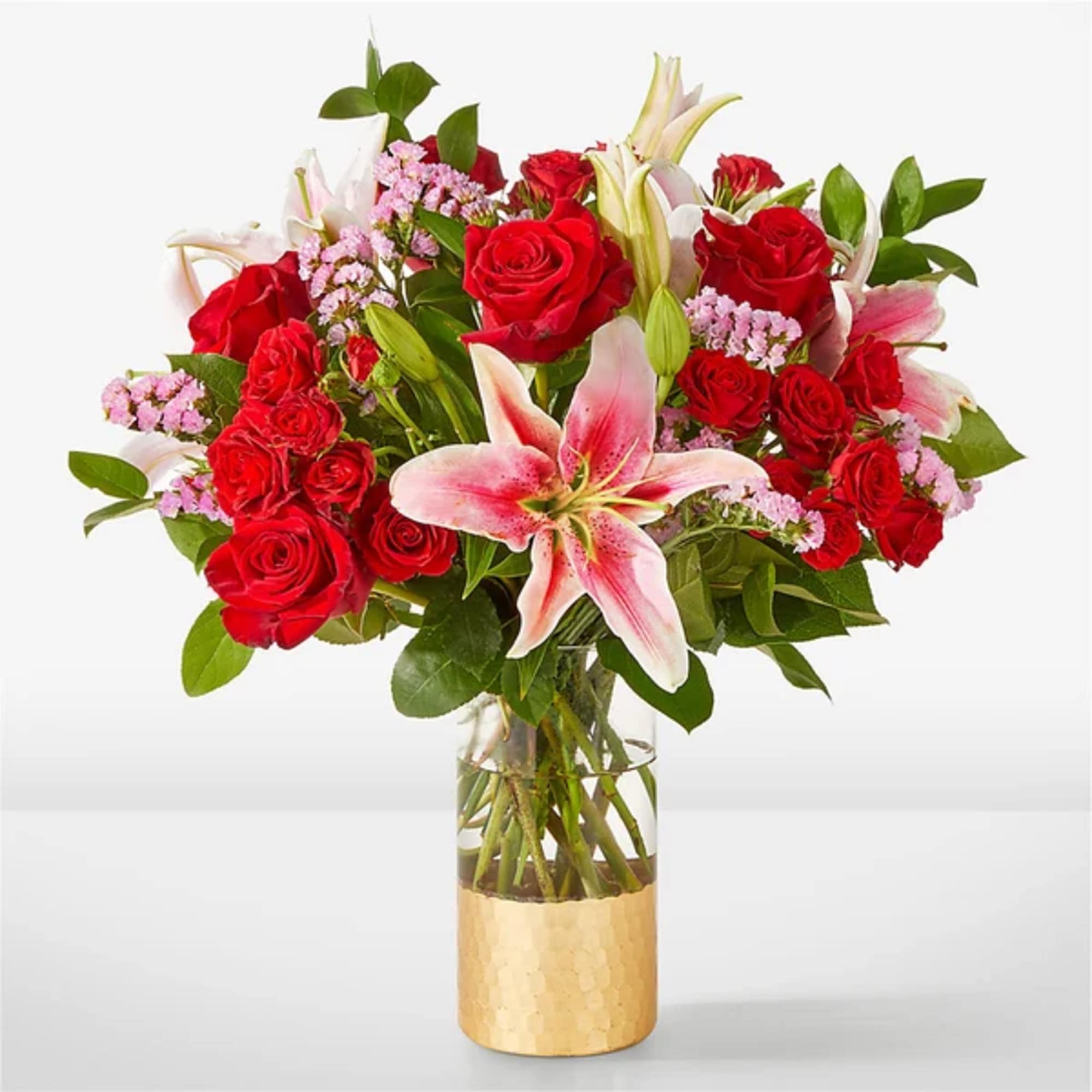 Red roses and pink lilies in a clear vase with a gold base