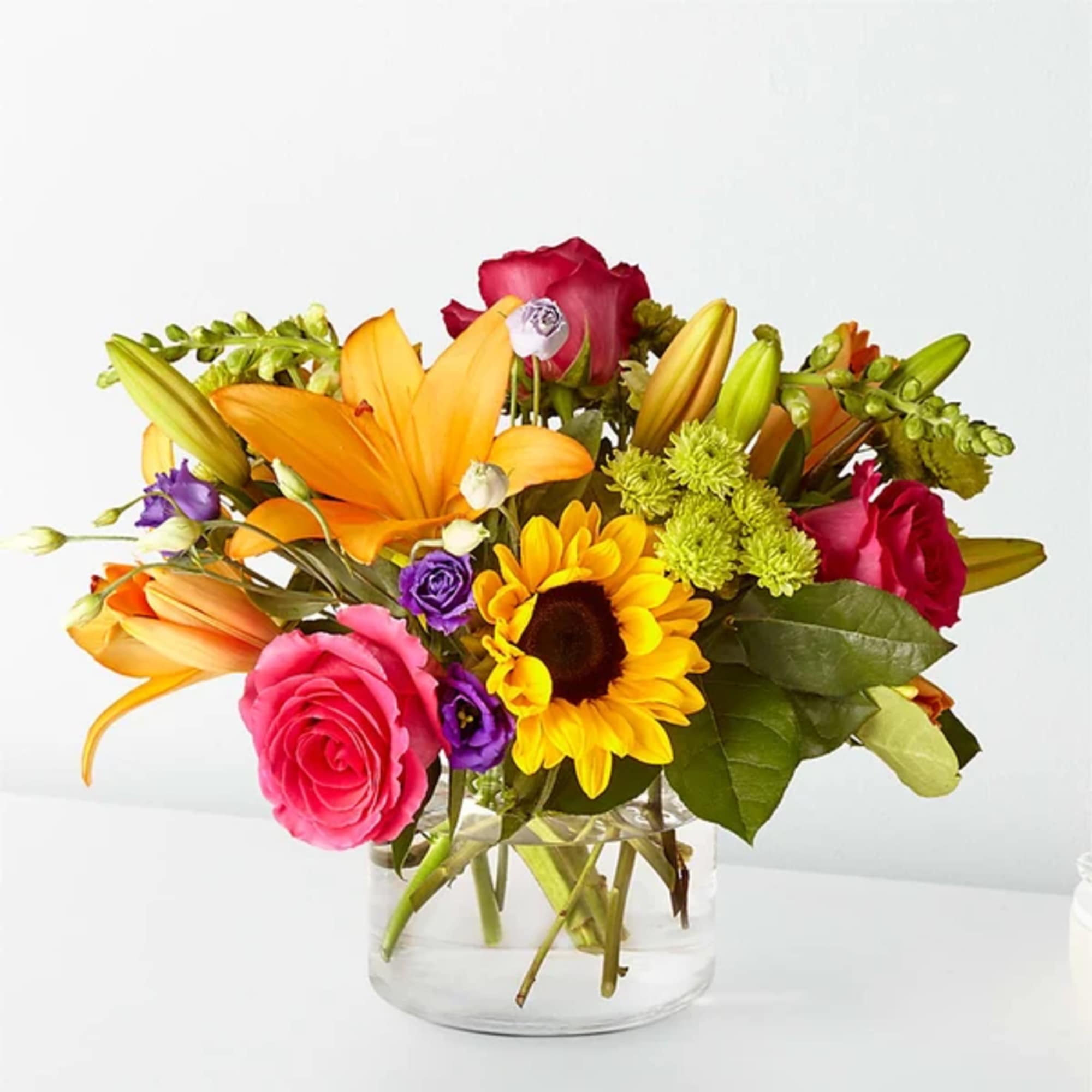 Mixed bouquet of roses, lilies, and a sunflower in a clear glass vase