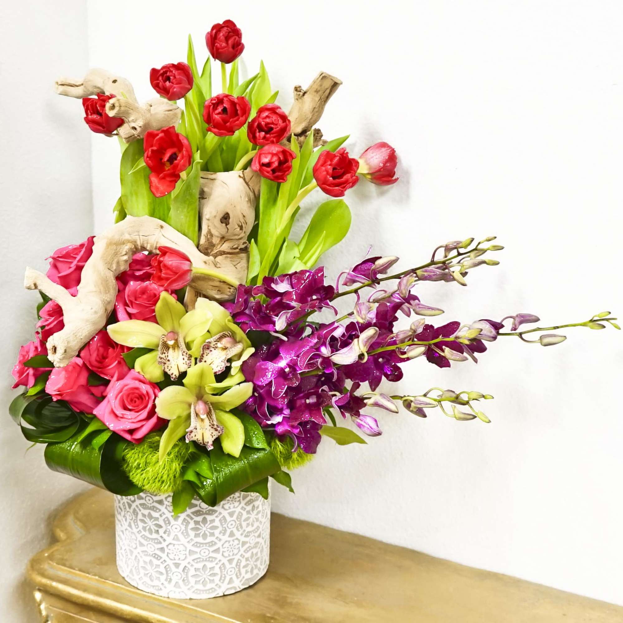Colorful floral arrangement in a white patterned vase with orchids and roses