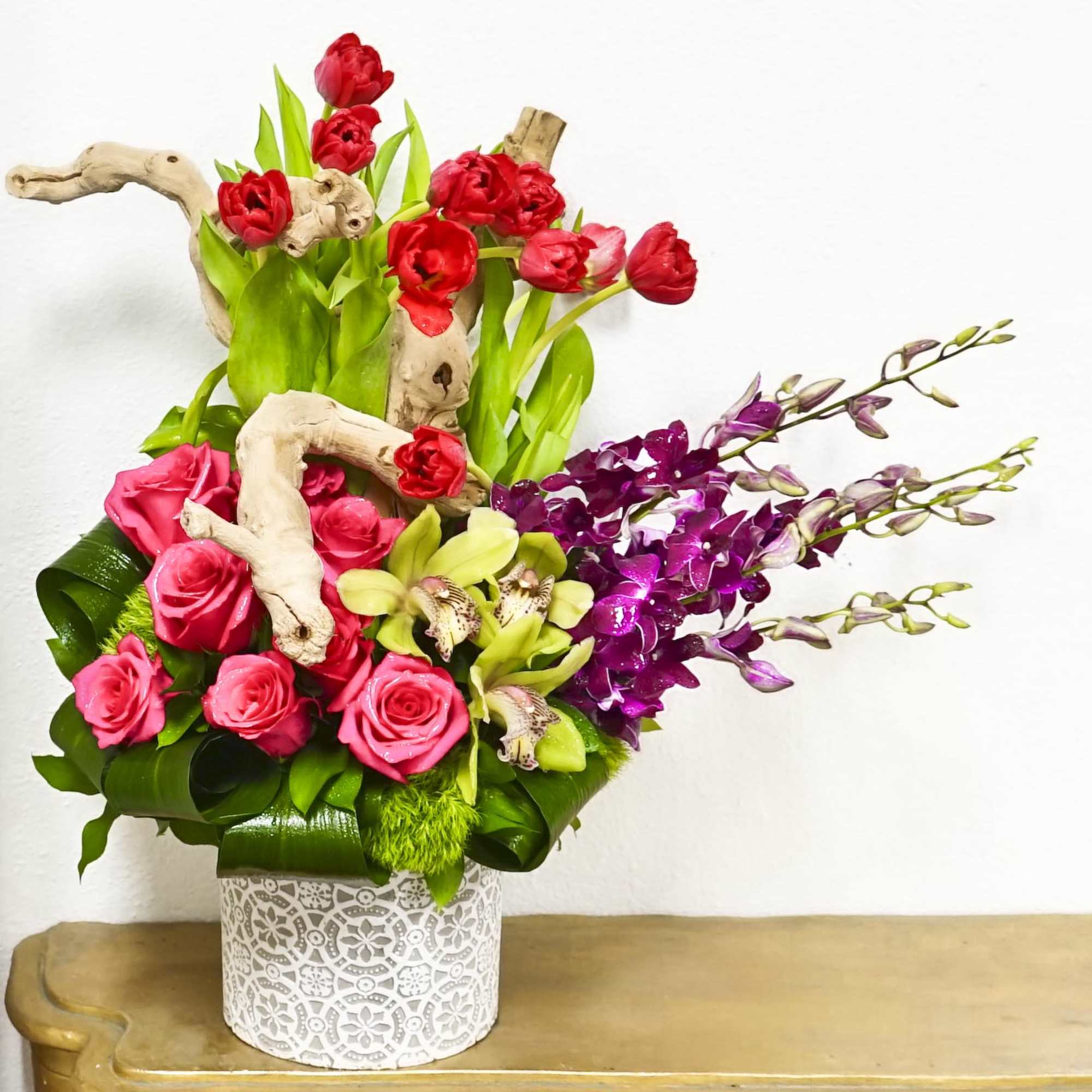 Pink and red roses with purple orchids in a white patterned vase