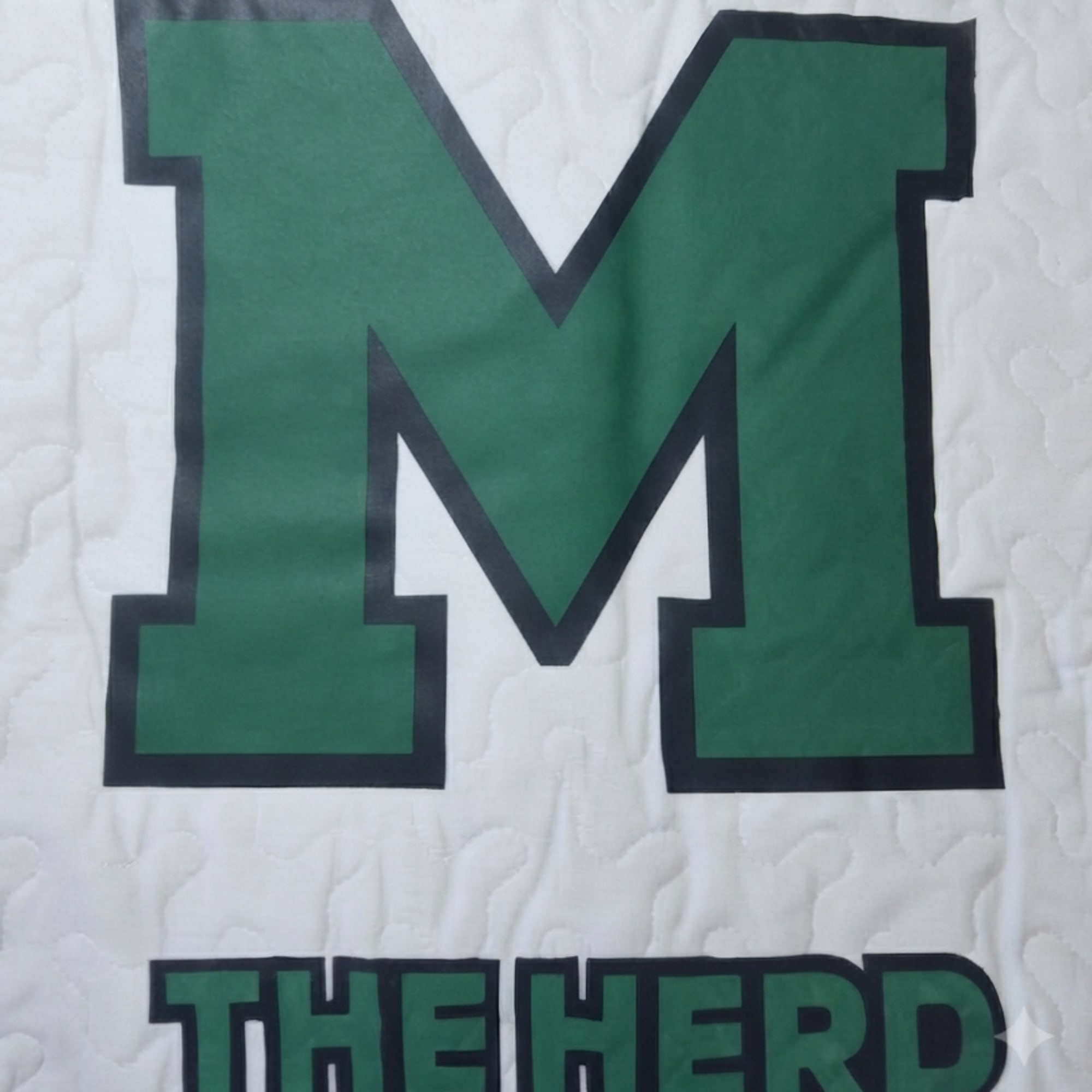 Green letter M with the words THE HERD on a white quilted background