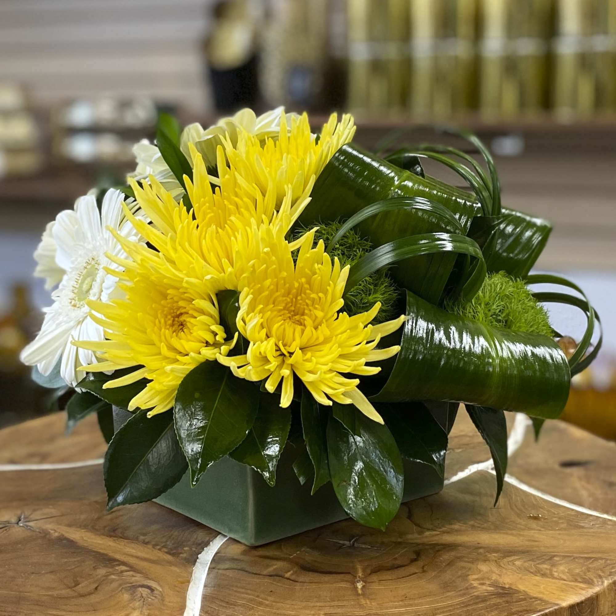 Yellow and white chrysanthemum arrangement in a square green container