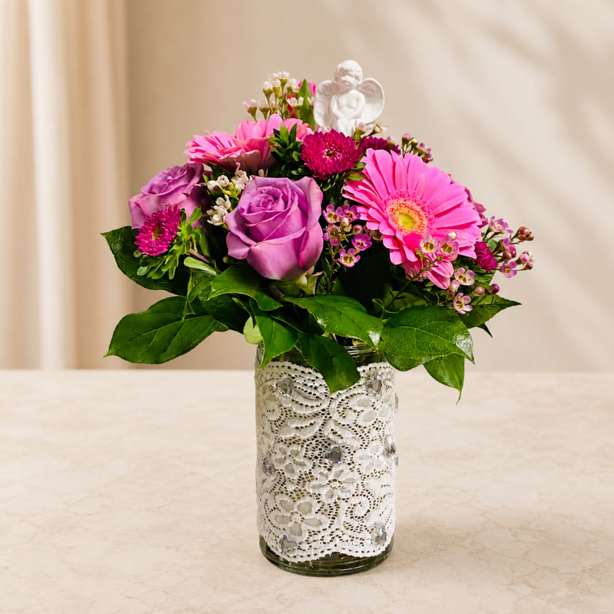Pink and purple flower arrangement in a lace-wrapped glass vase