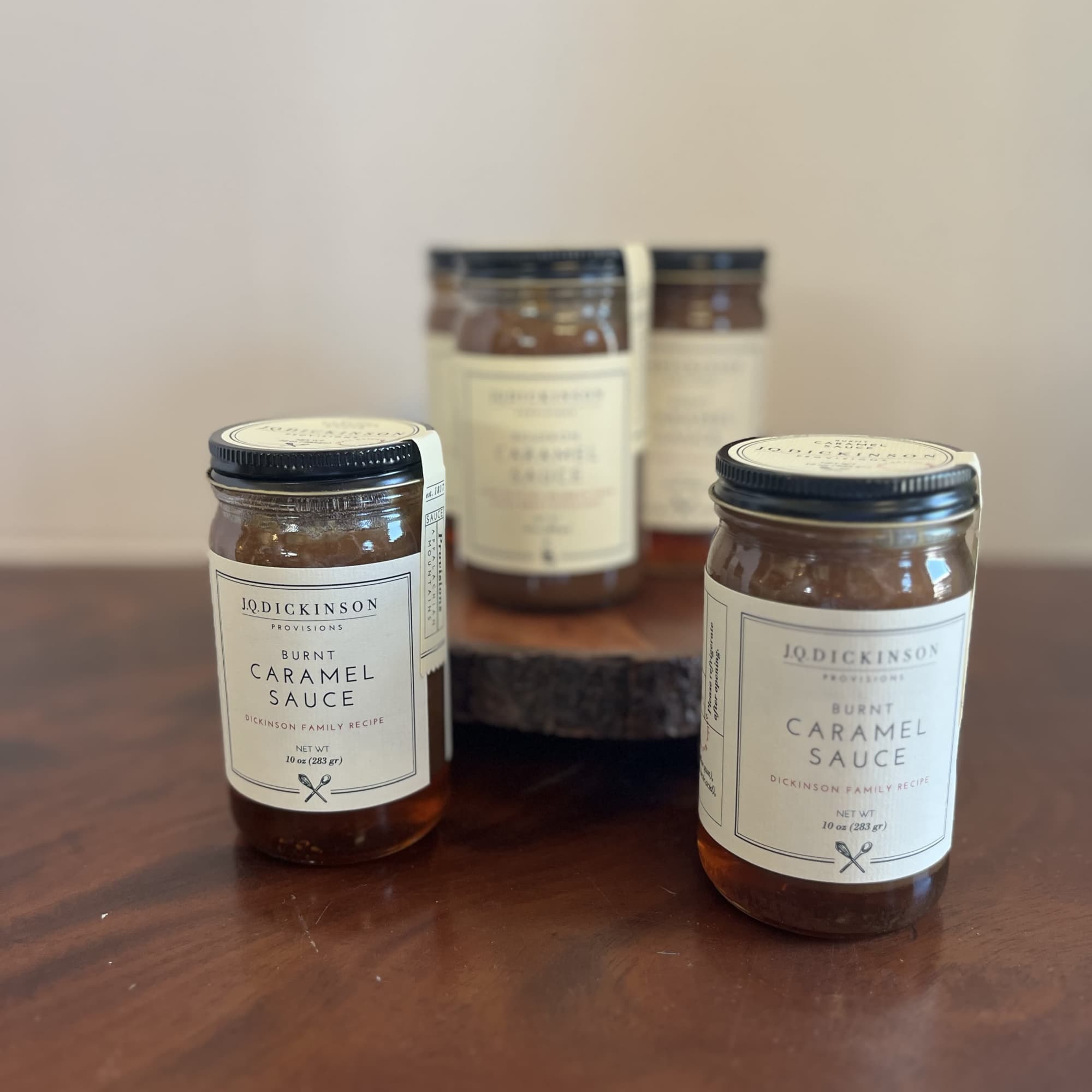 Group of jars of burnt caramel sauce on a wooden surface with one raised on a wood stand