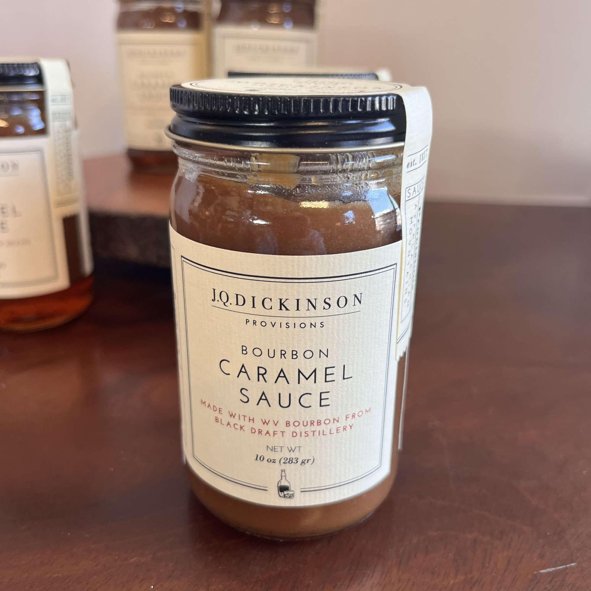 Jar of bourbon caramel sauce with cream label and black lid on a wooden surface