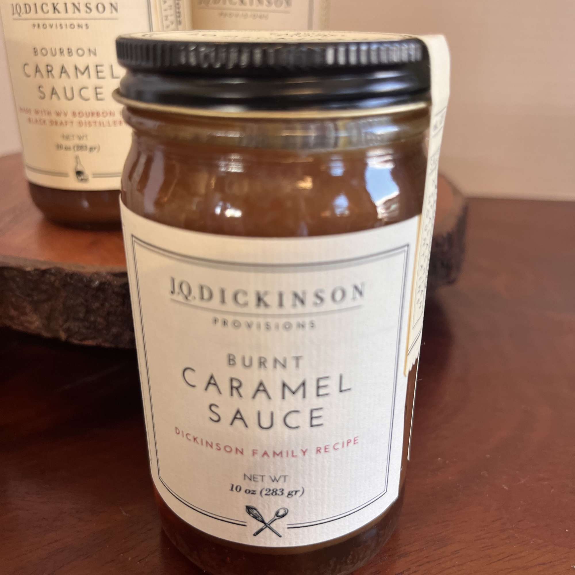 Glass jar of burnt caramel sauce with cream label and black lid on wooden surface