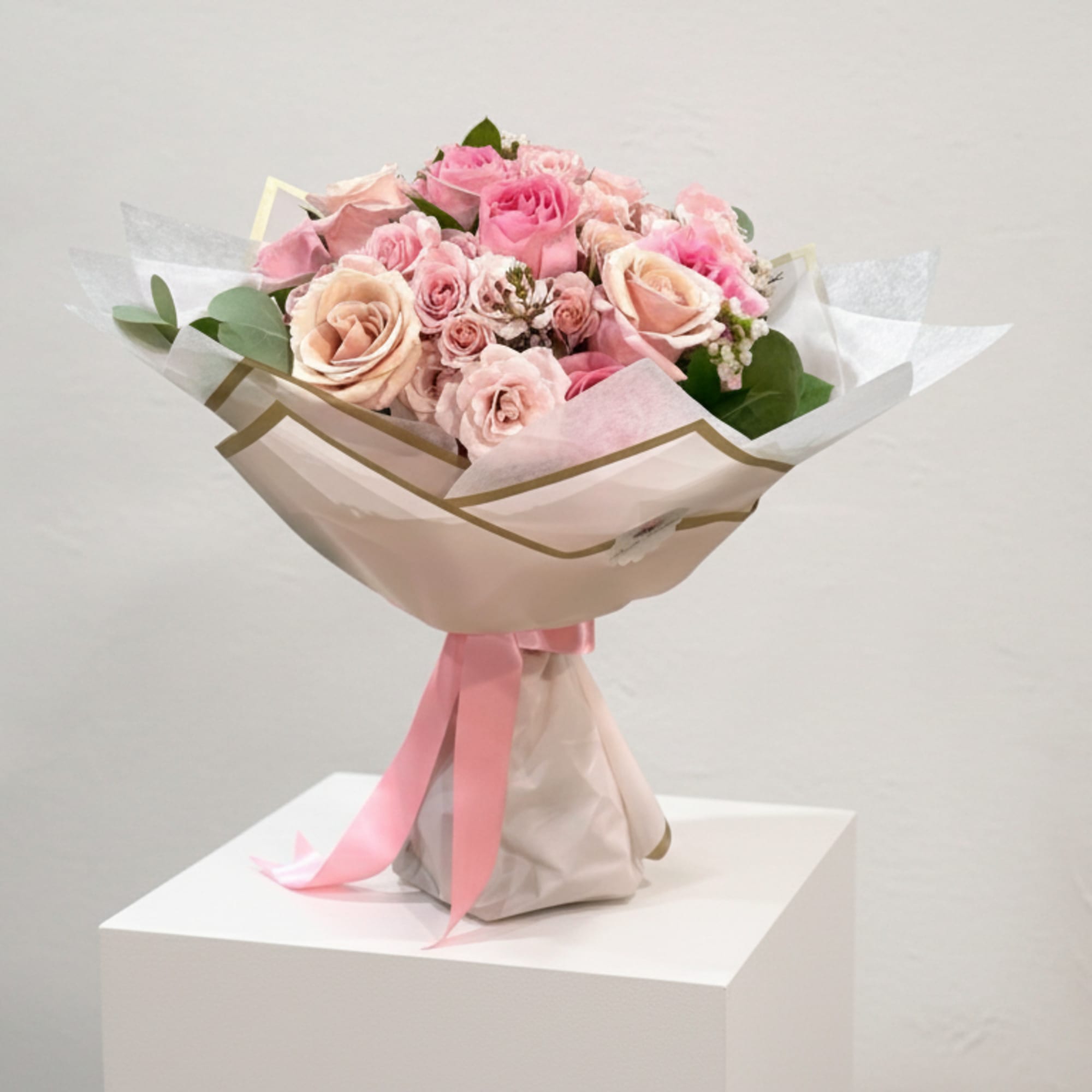 Pink and blush rose bouquet wrapped in pale paper with a pink ribbon