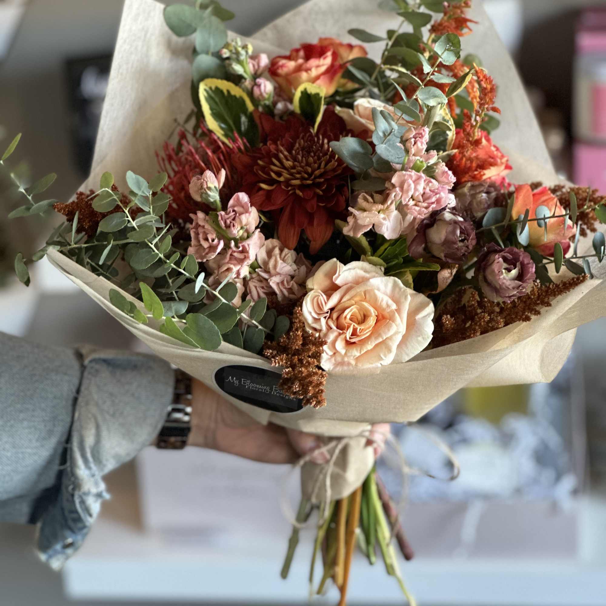 Hand-tied bouquet of peach, red, and pink flowers wrapped in kraft paper