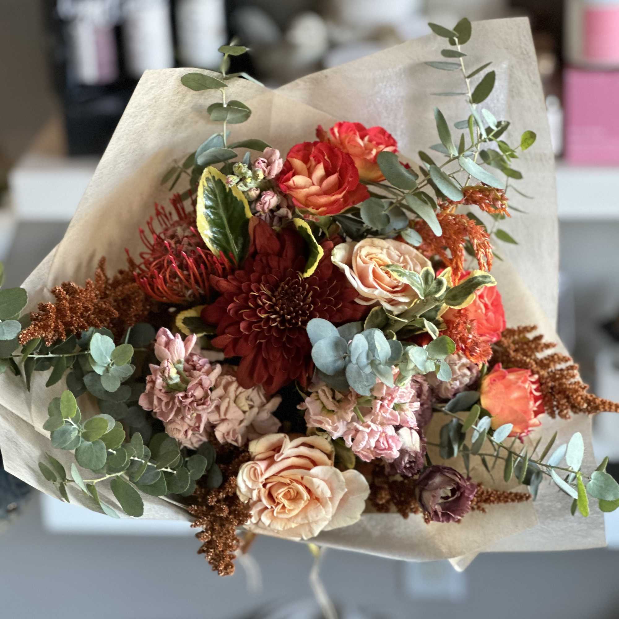 Hand-tied bouquet of red, peach, and pink flowers wrapped in beige paper