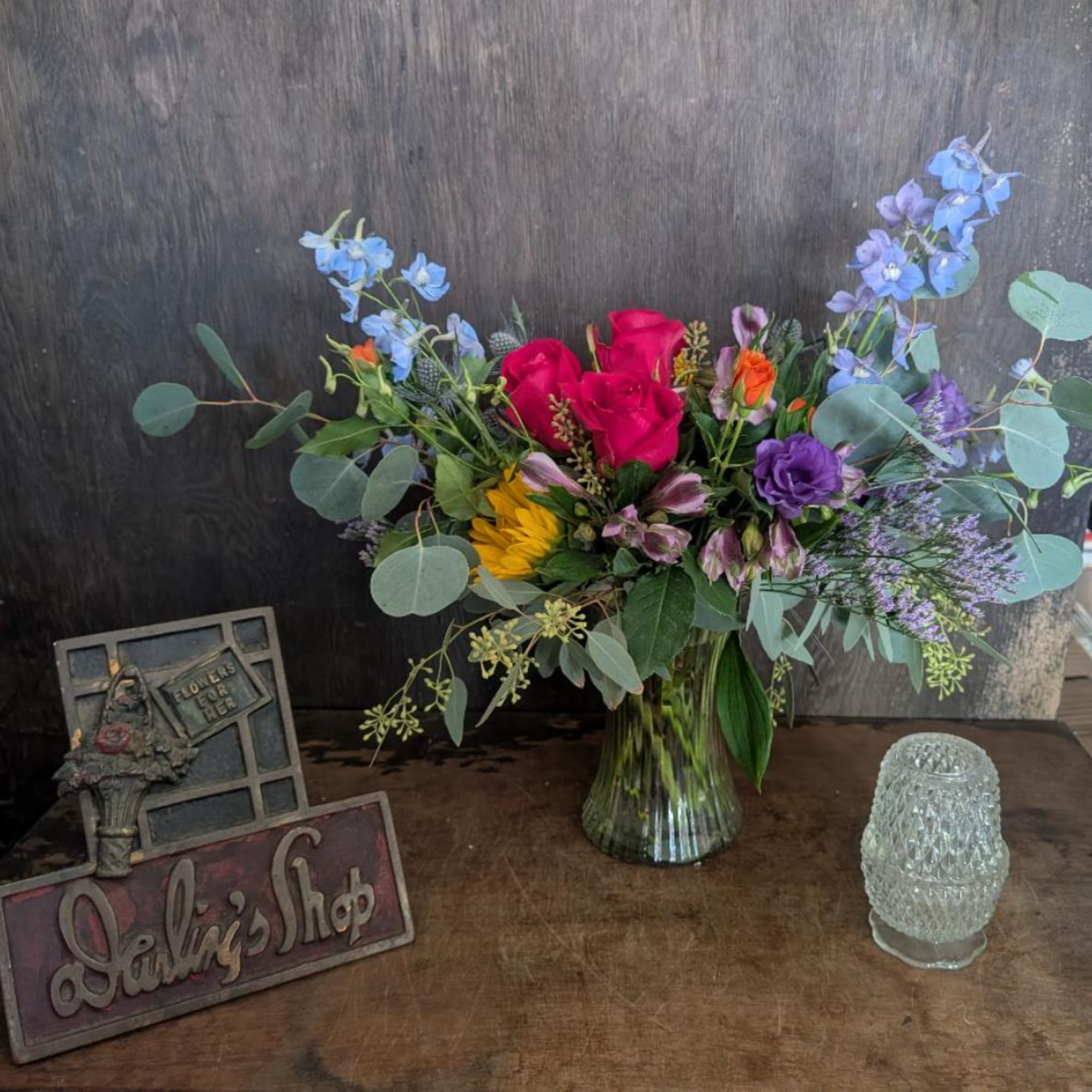 Mixed bouquet of roses, sunflowers, and blue flowers in a glass vase