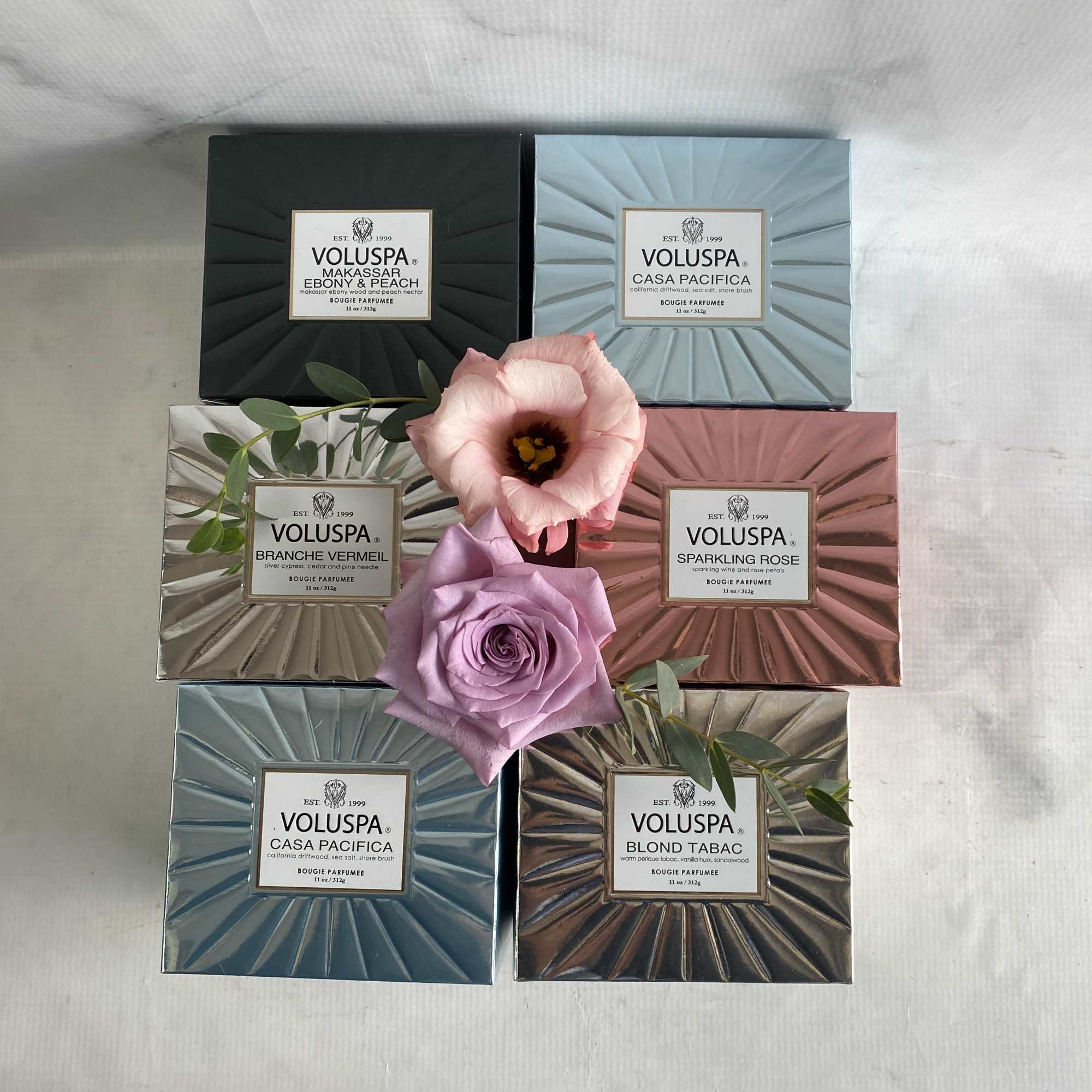 Five Voluspa candle boxes arranged with two flowers in the center