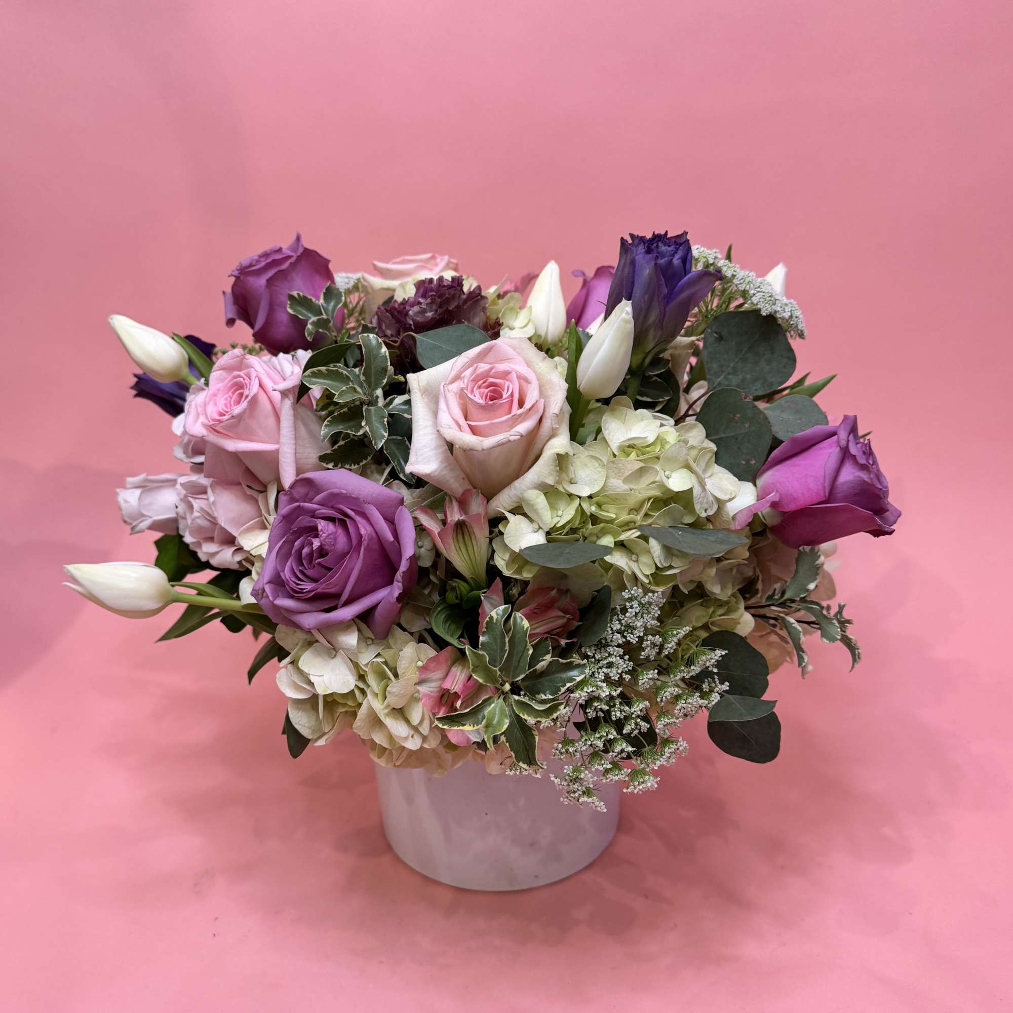 Bouquet of pink and purple roses with white tulips in a white vase