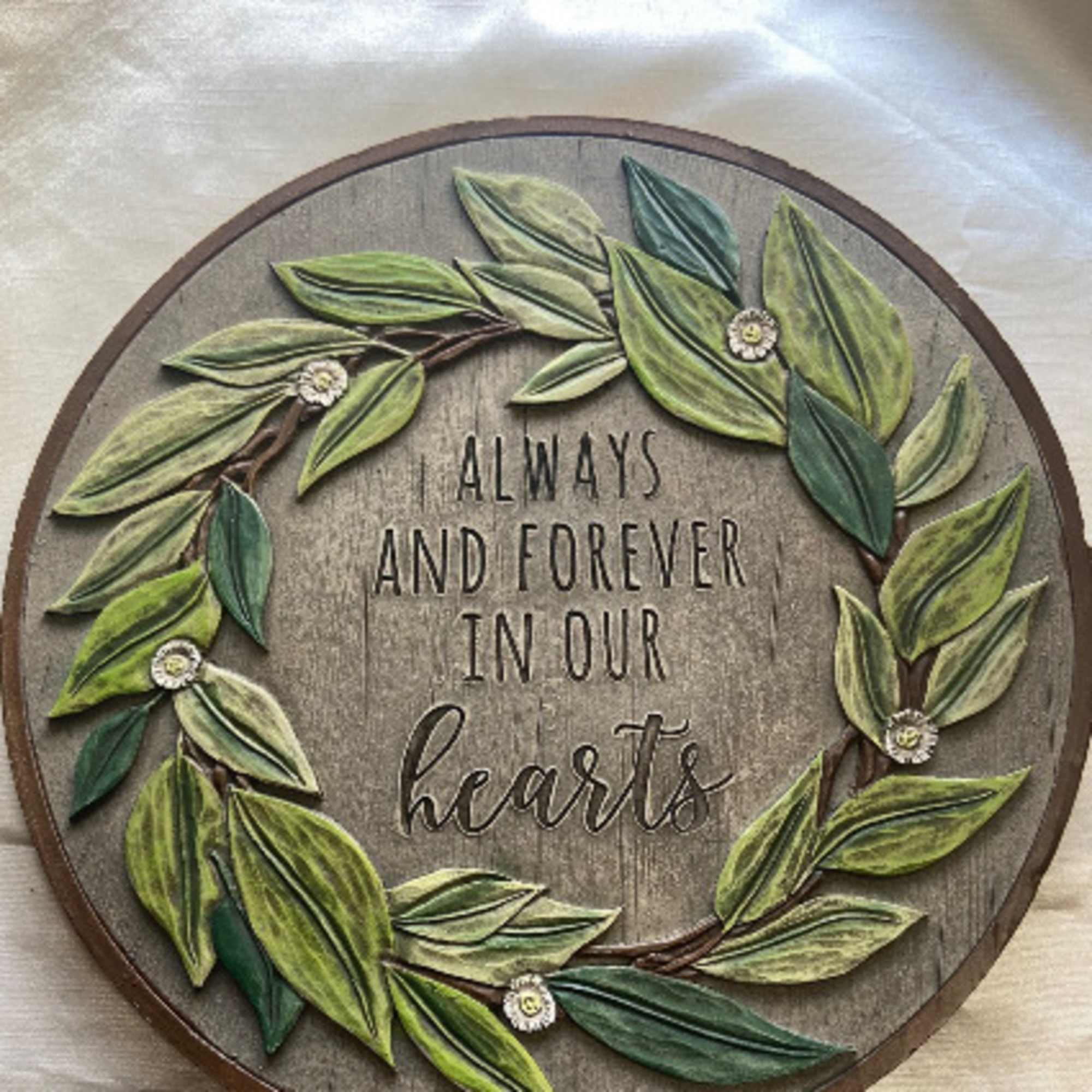 Round wooden wall sign with leafy wreath and the words "Always and Forever in Our Hearts"