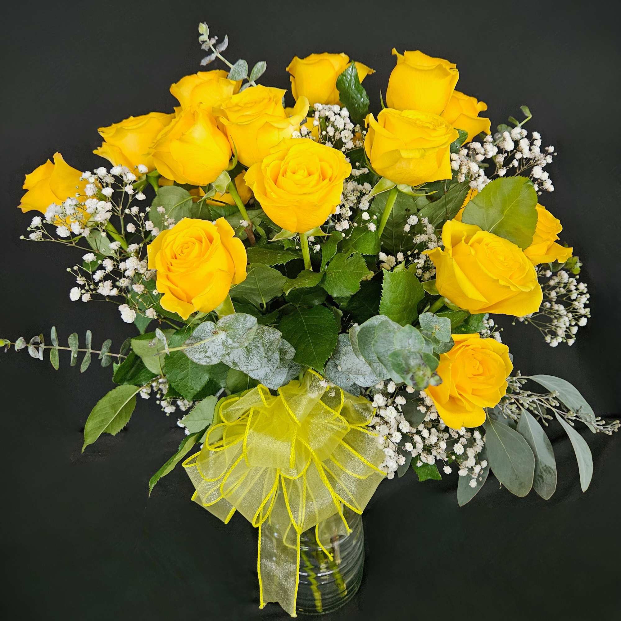 Arrangement of bright yellow roses with white baby's breath in a glass vase with a yellow bow