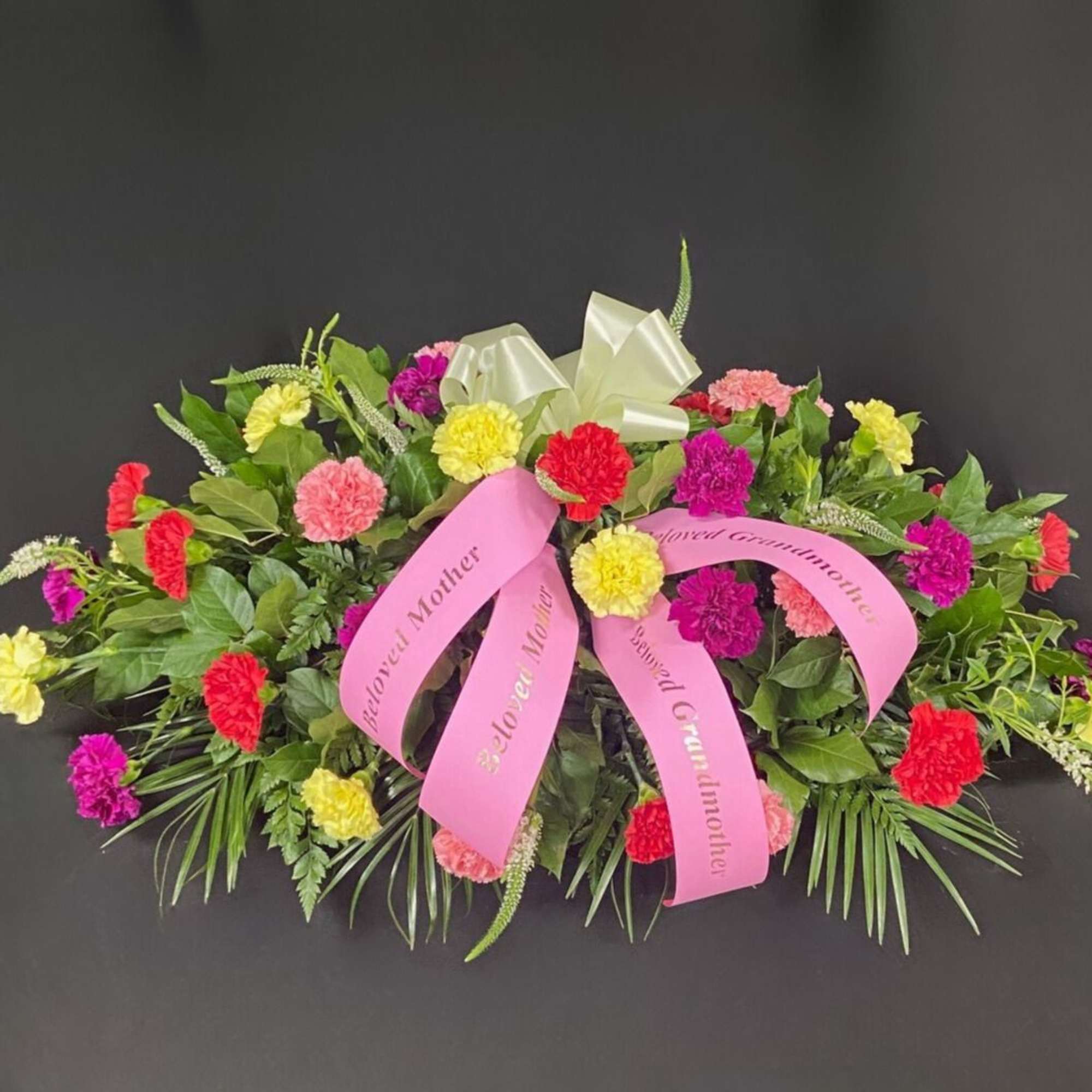 Colorful carnation funeral spray with pink ribbons on a dark background