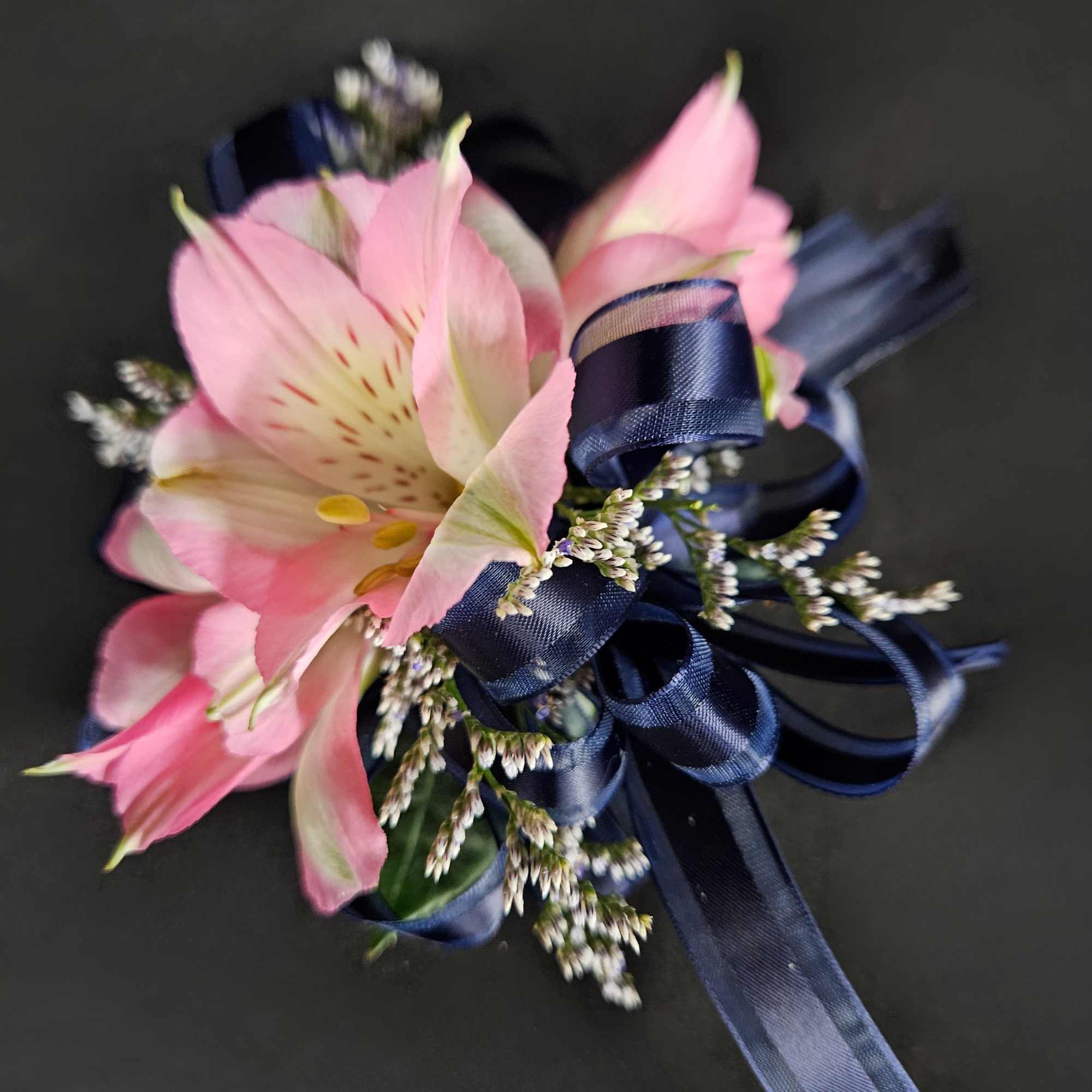 Pink alstroemeria corsage with navy ribbon on a dark background