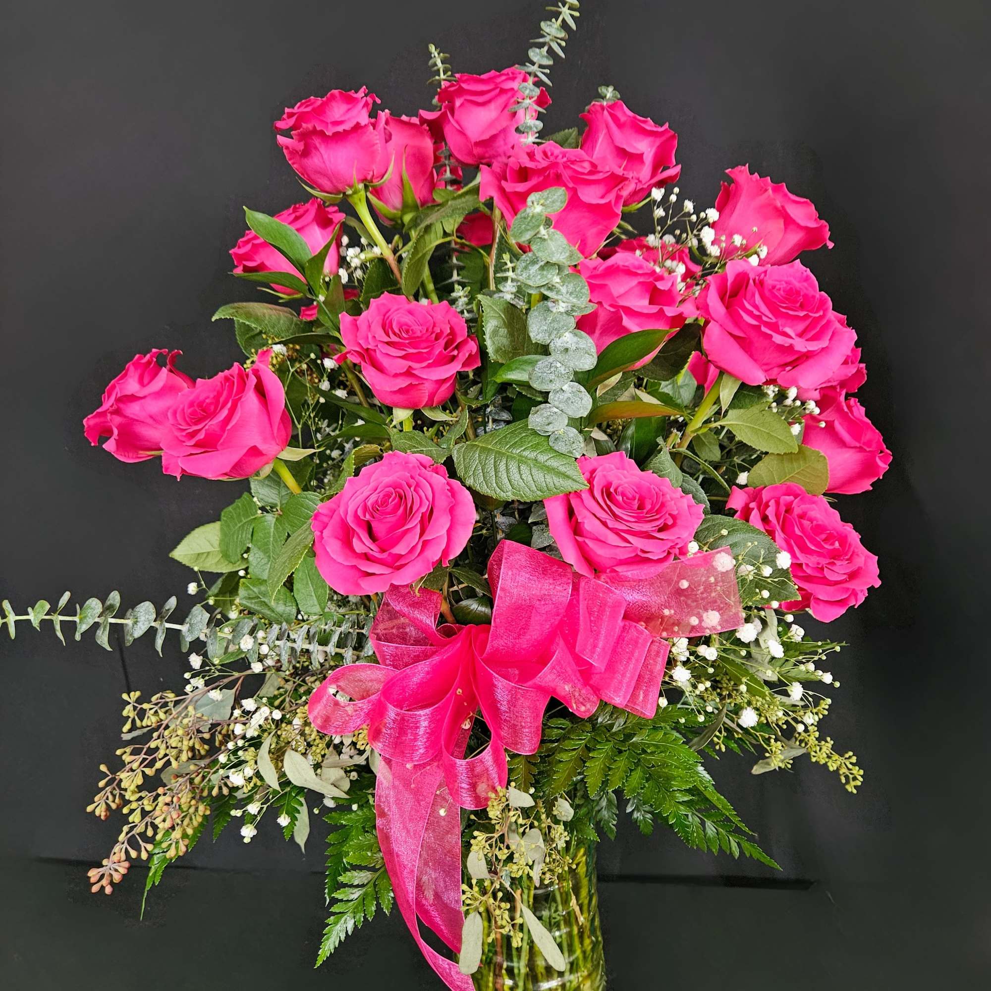 Bright pink roses in a glass vase with a pink ribbon.