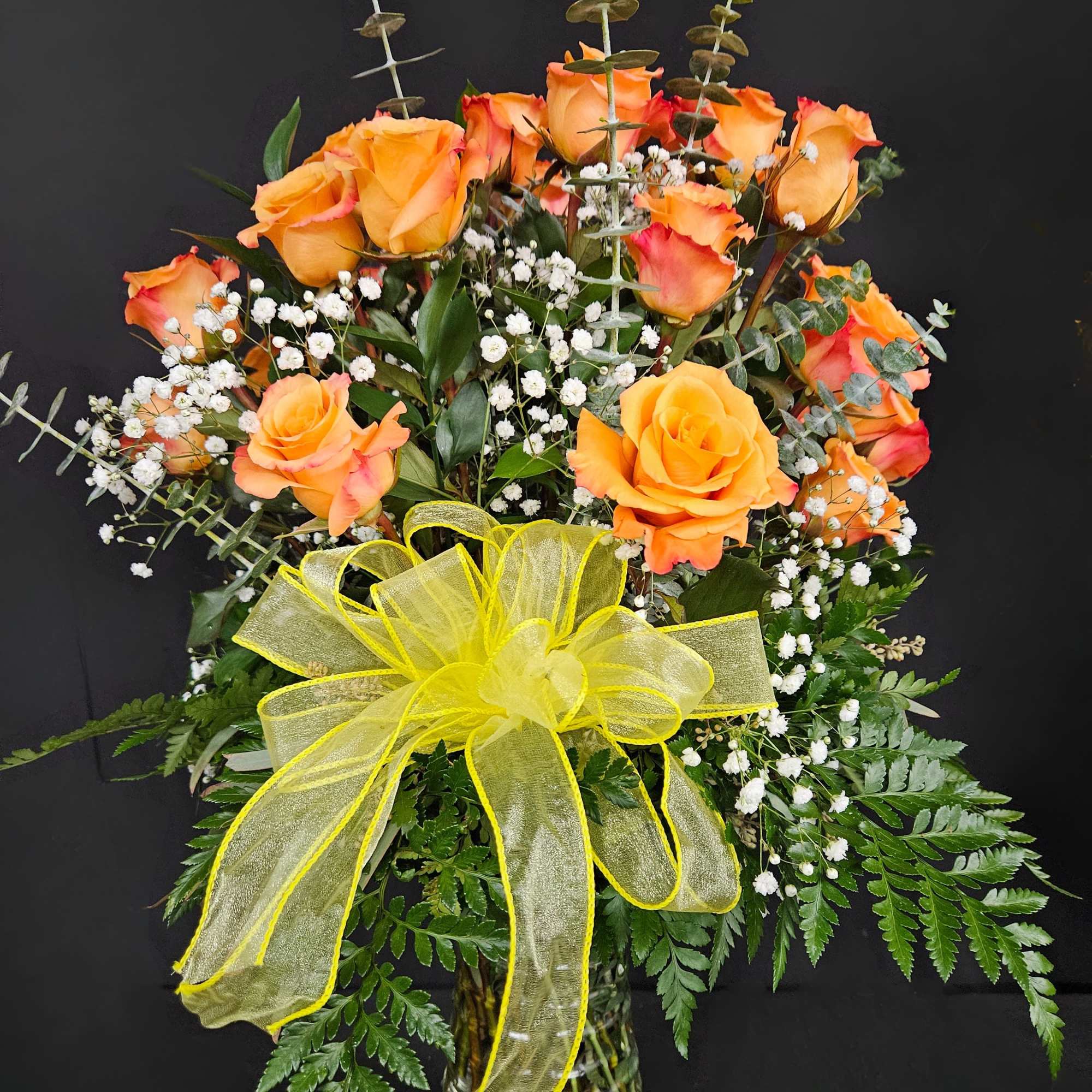 Orange roses in a glass vase with a yellow bow