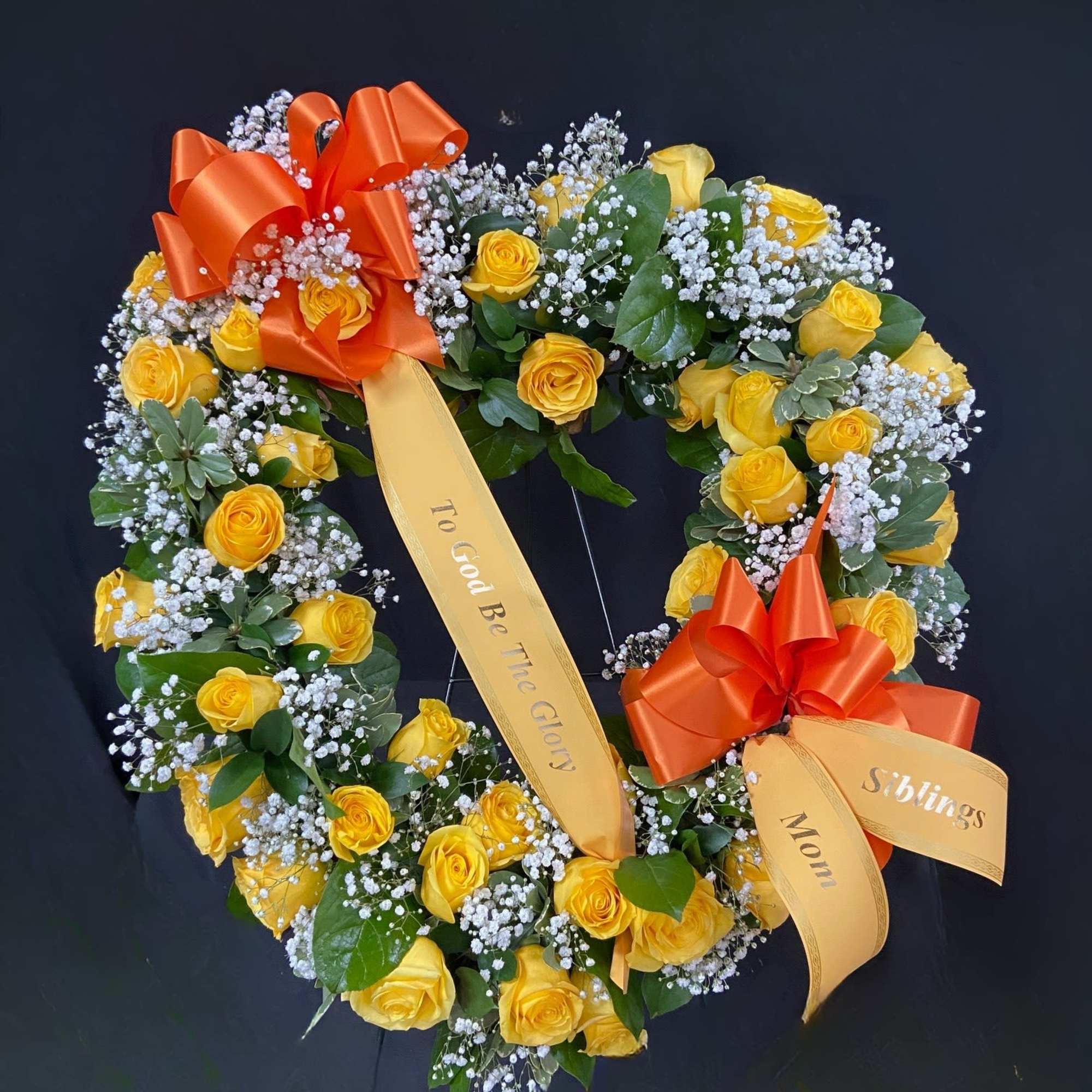 Heart-shaped wreath of yellow roses with orange ribbons on a dark background