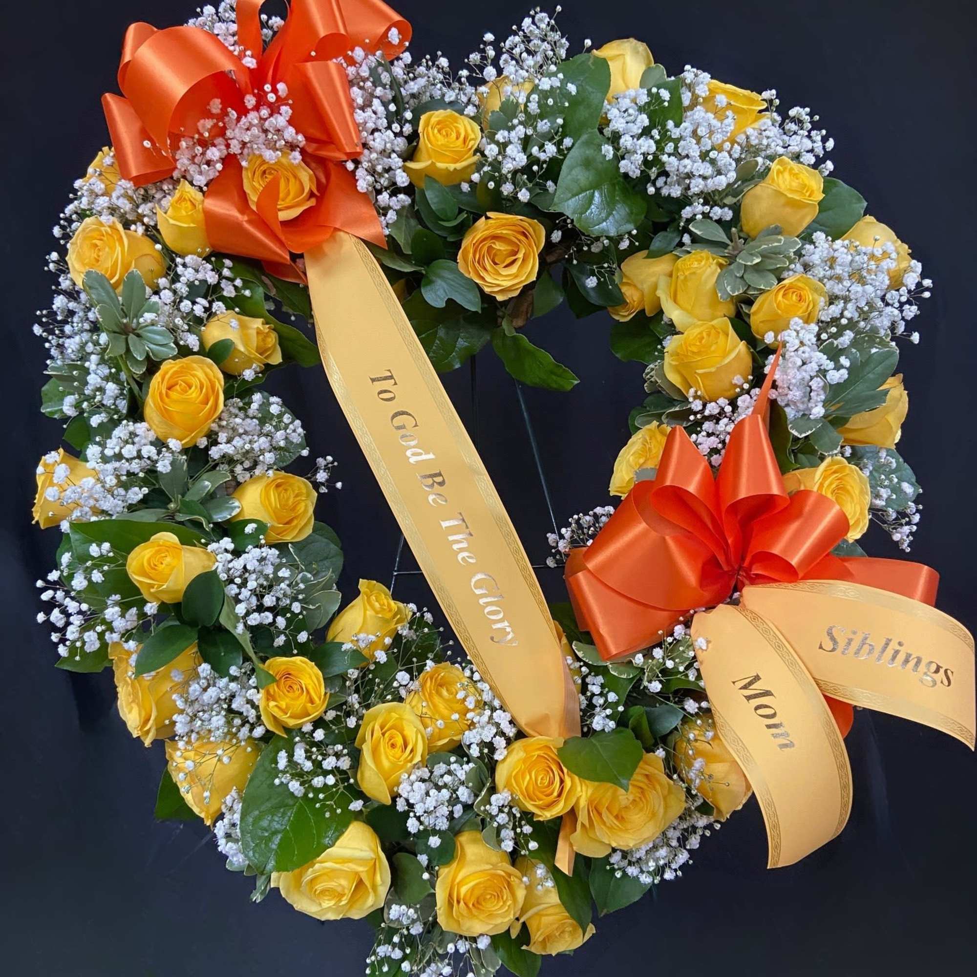 Heart-shaped wreath of yellow roses with orange bows and ribbons
