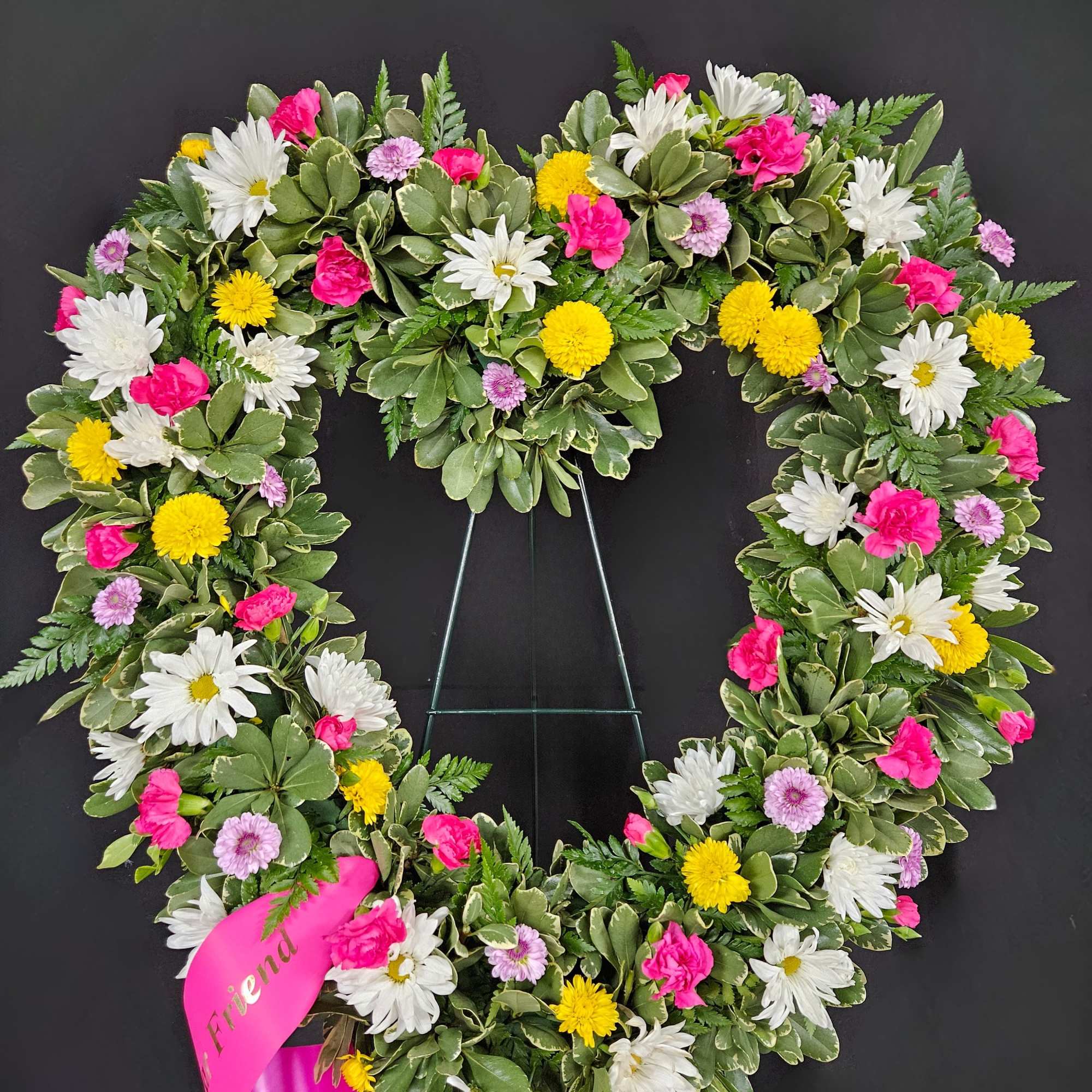 Heart-shaped floral wreath with pink, white, and yellow blooms on a stand
