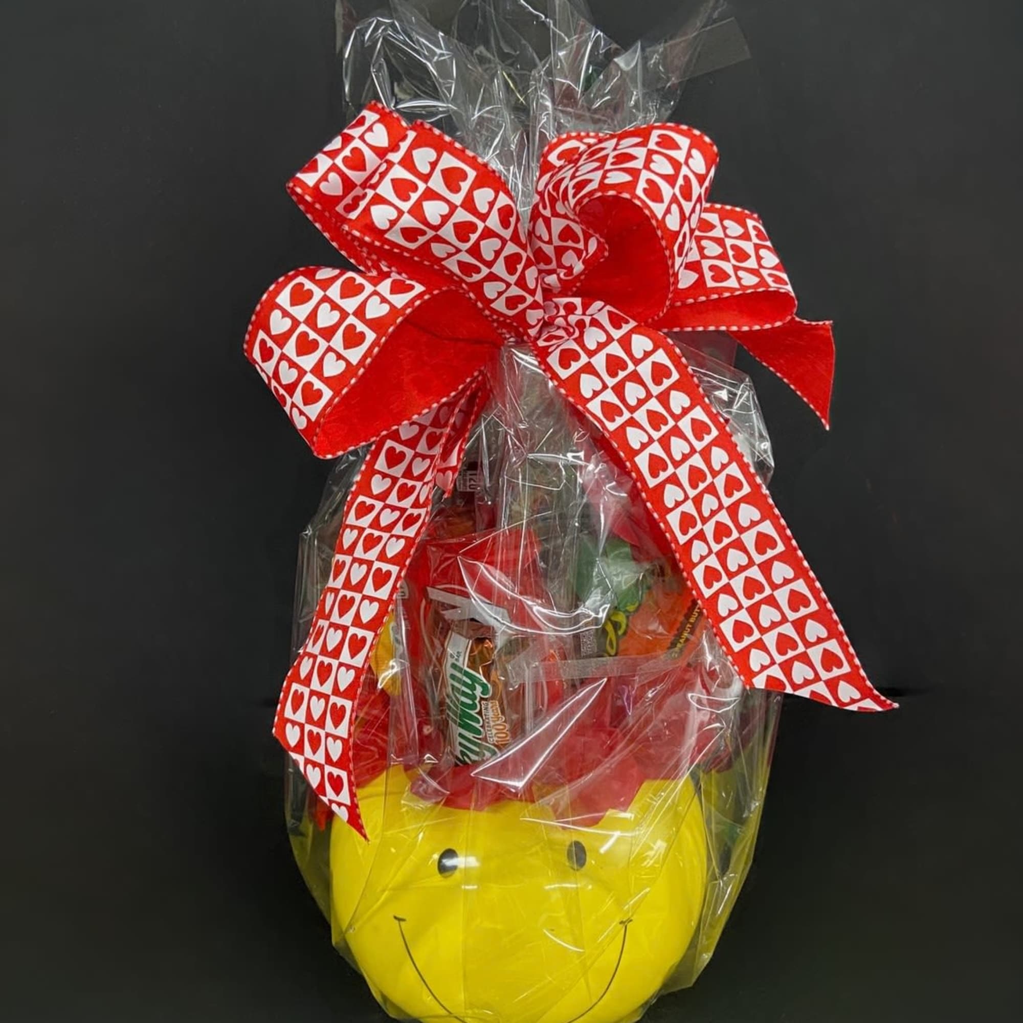 Gift basket wrapped in cellophane with a red heart ribbon and smiley-face container