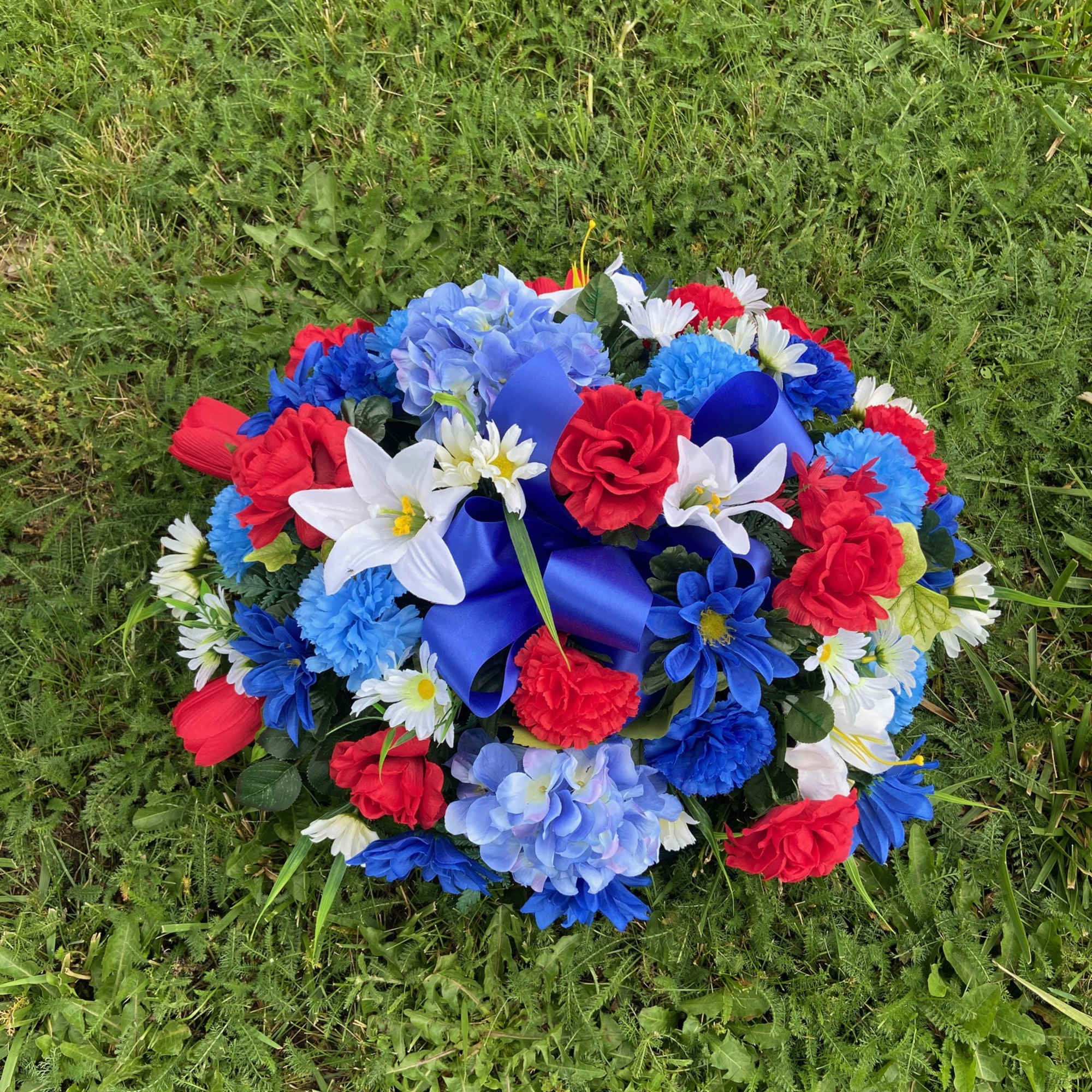 Round bouquet of red, blue, and white flowers with a blue ribbon