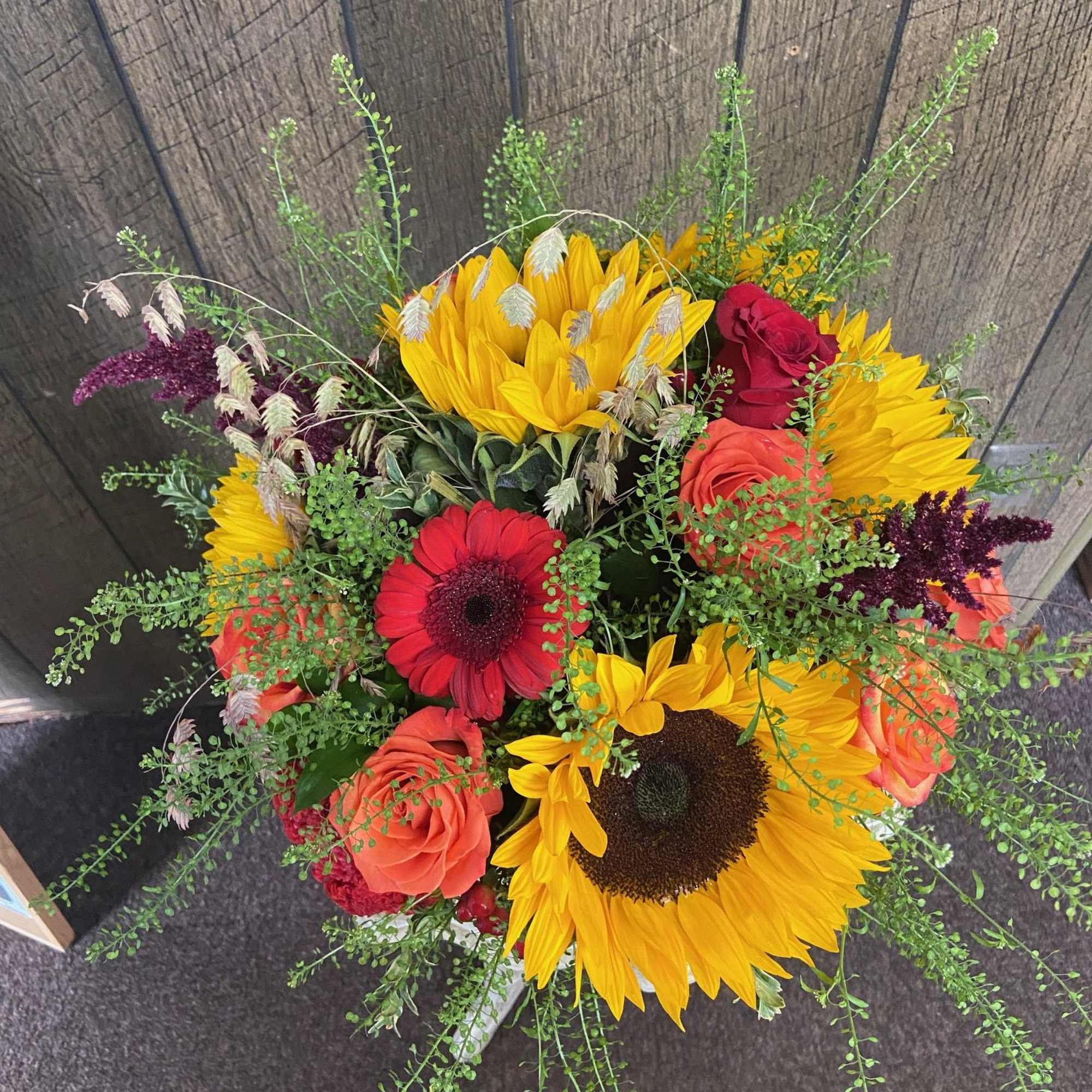 Arrangement of sunflowers, red gerbera daisies, roses and airy greenery in a vase.