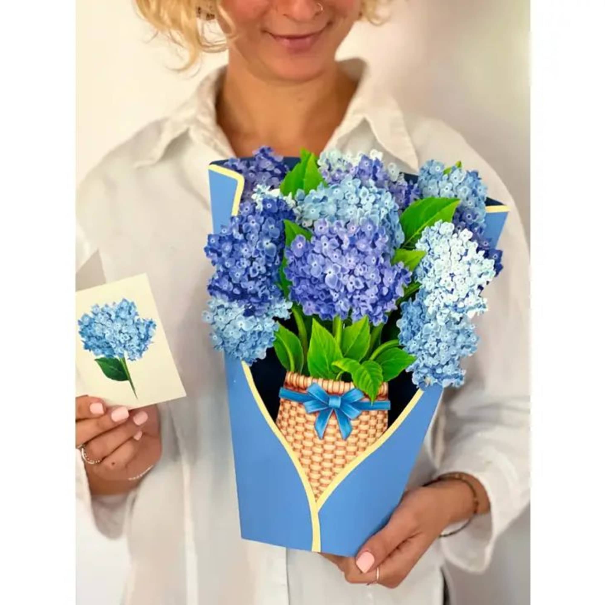 Person holding a blue pop-up bouquet card of blue flowers with a matching small card.