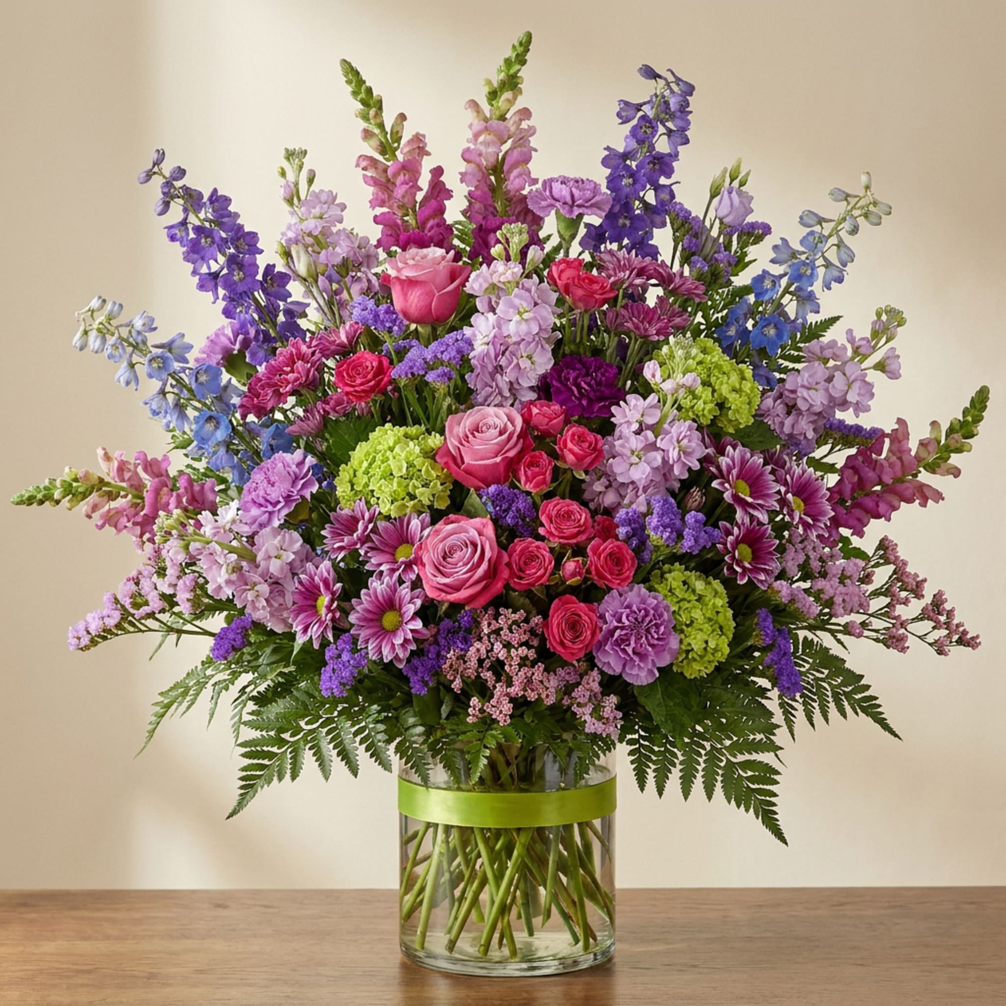 Mixed pink, purple, and blue flowers in a clear glass vase with a green ribbon