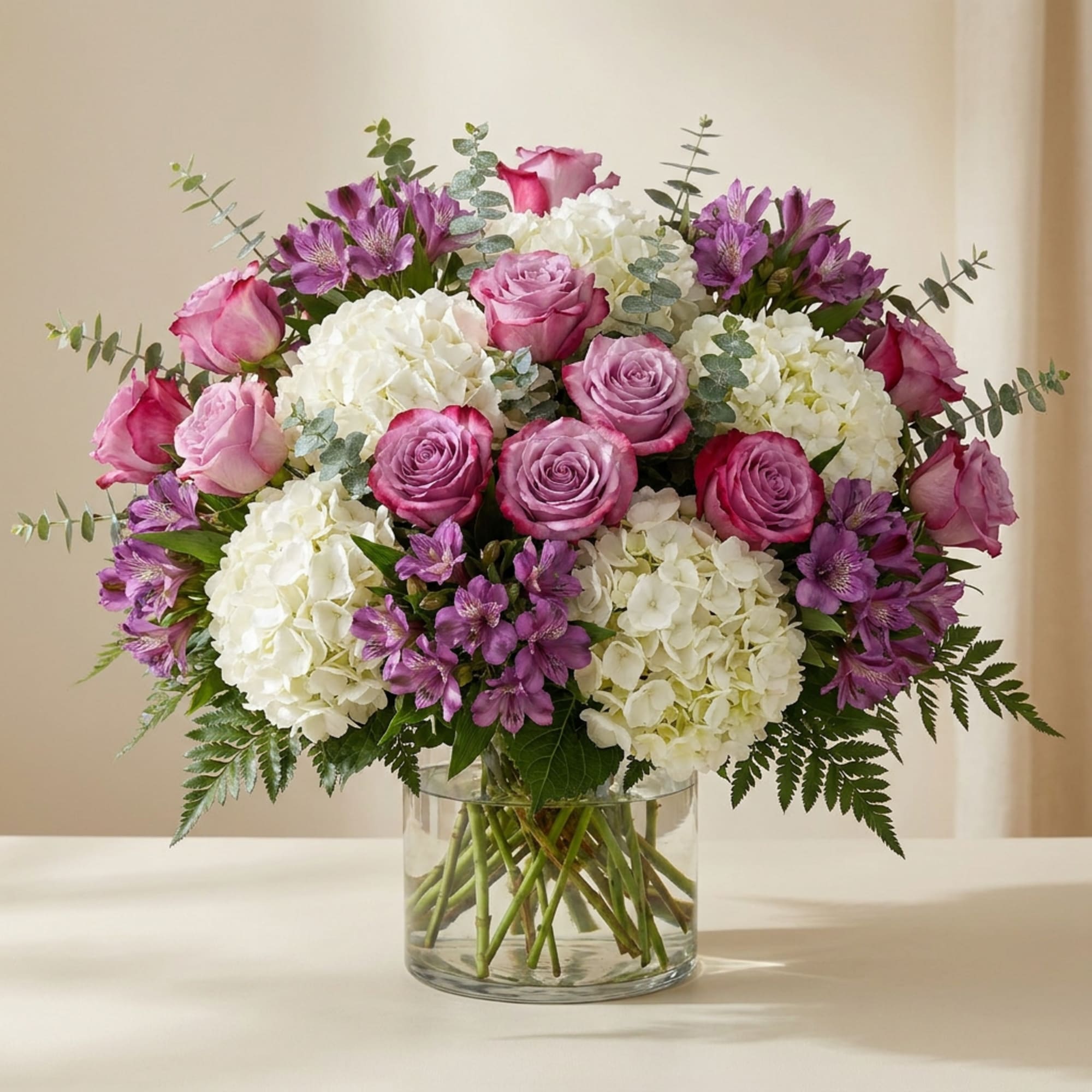 Pink roses and purple flowers arranged with white hydrangeas in a glass vase.