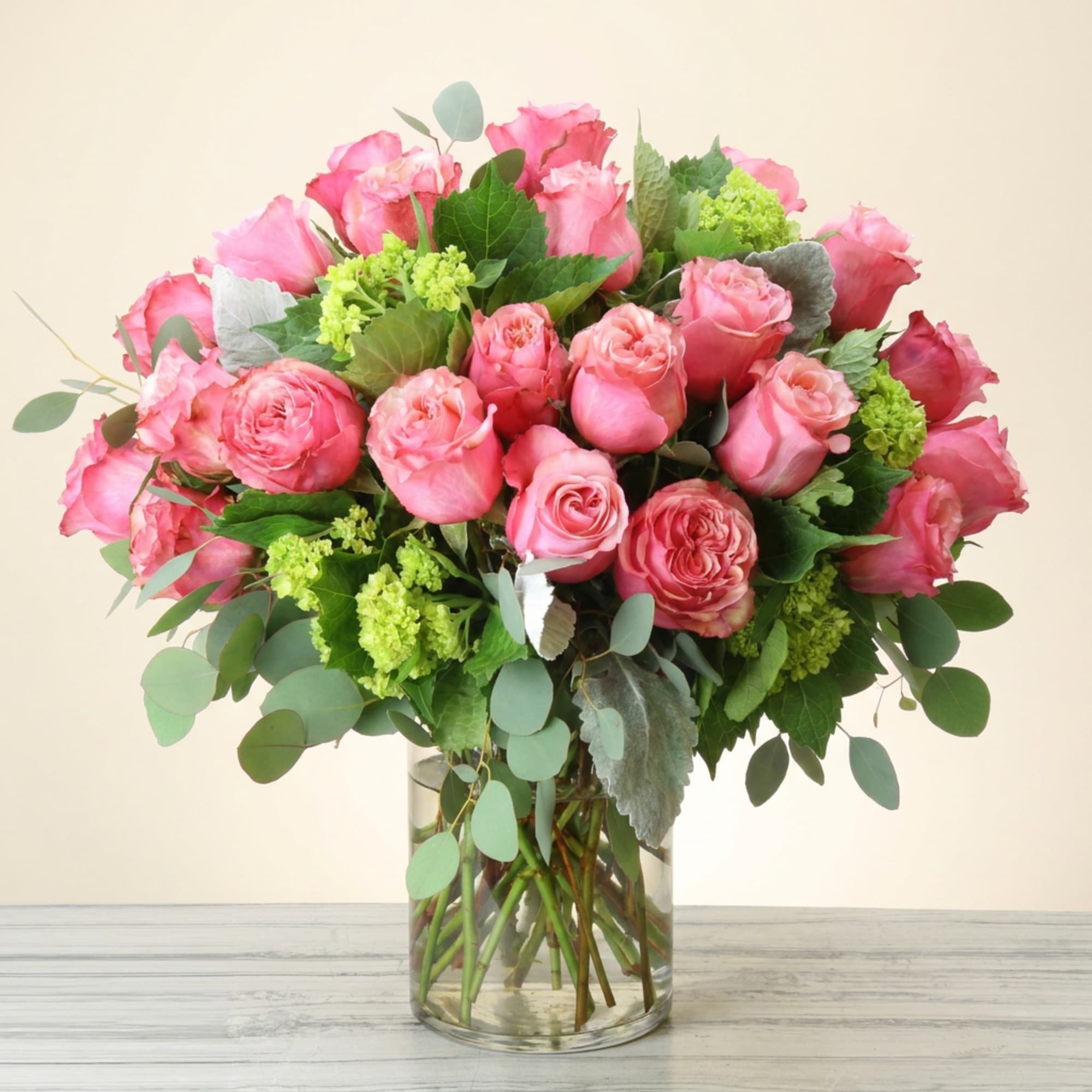 Pink roses arranged in a clear glass vase with green filler and eucalyptus
