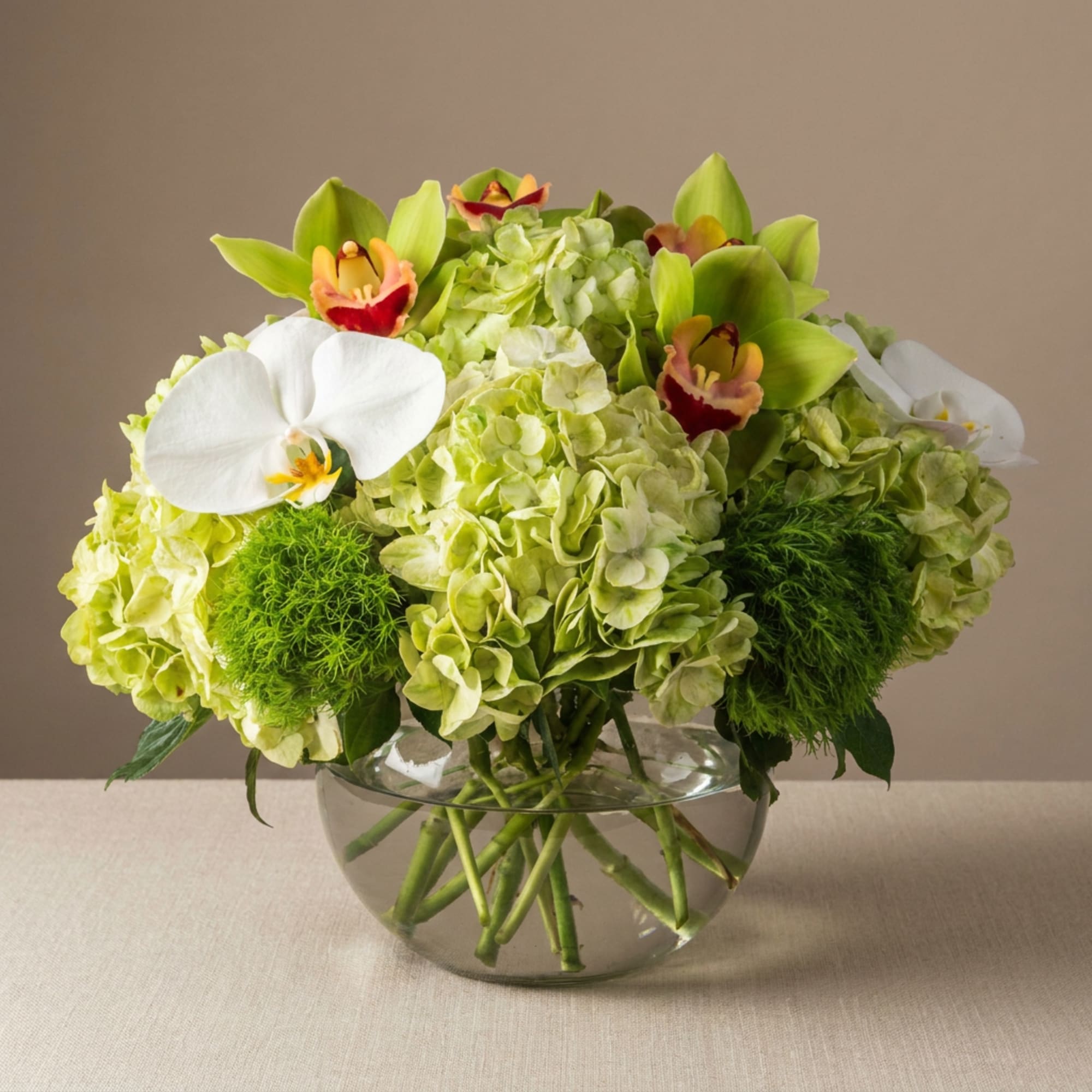 Green hydrangea arrangement with white orchids in a clear glass bowl