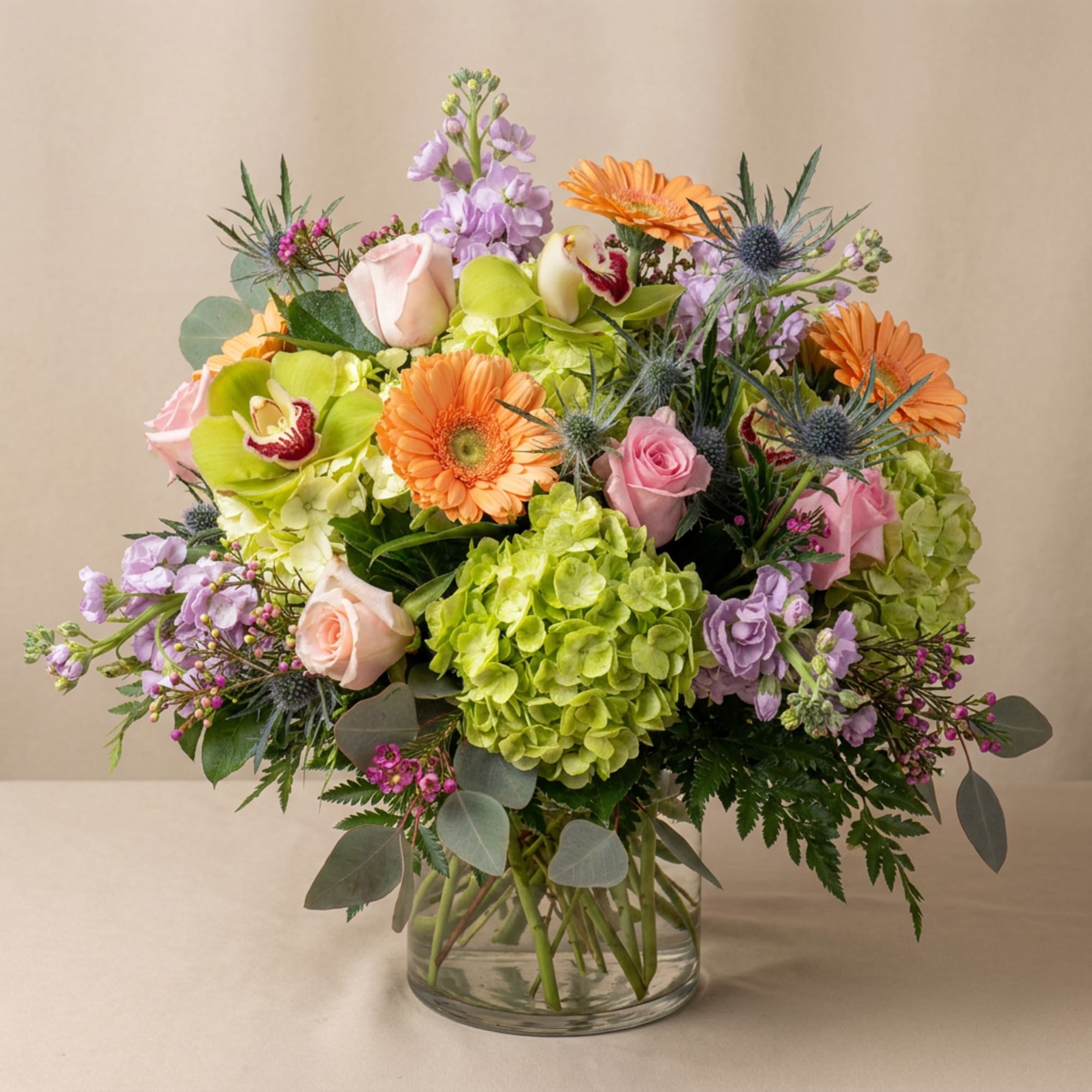 Mixed bouquet with pink roses, orange gerberas, and green hydrangea in a glass vase