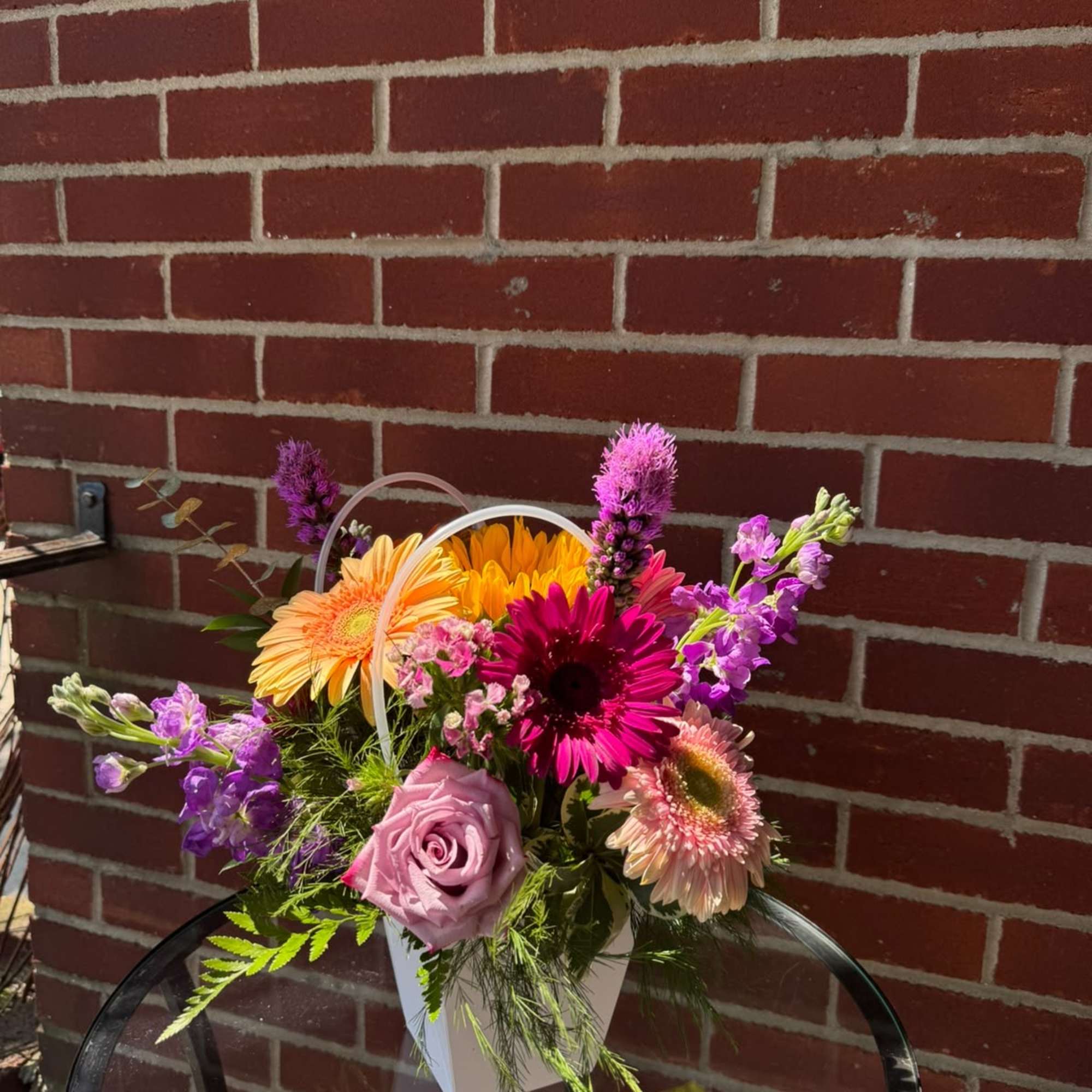 Mixed bouquet in a white handled container with pink, purple, and orange flowers