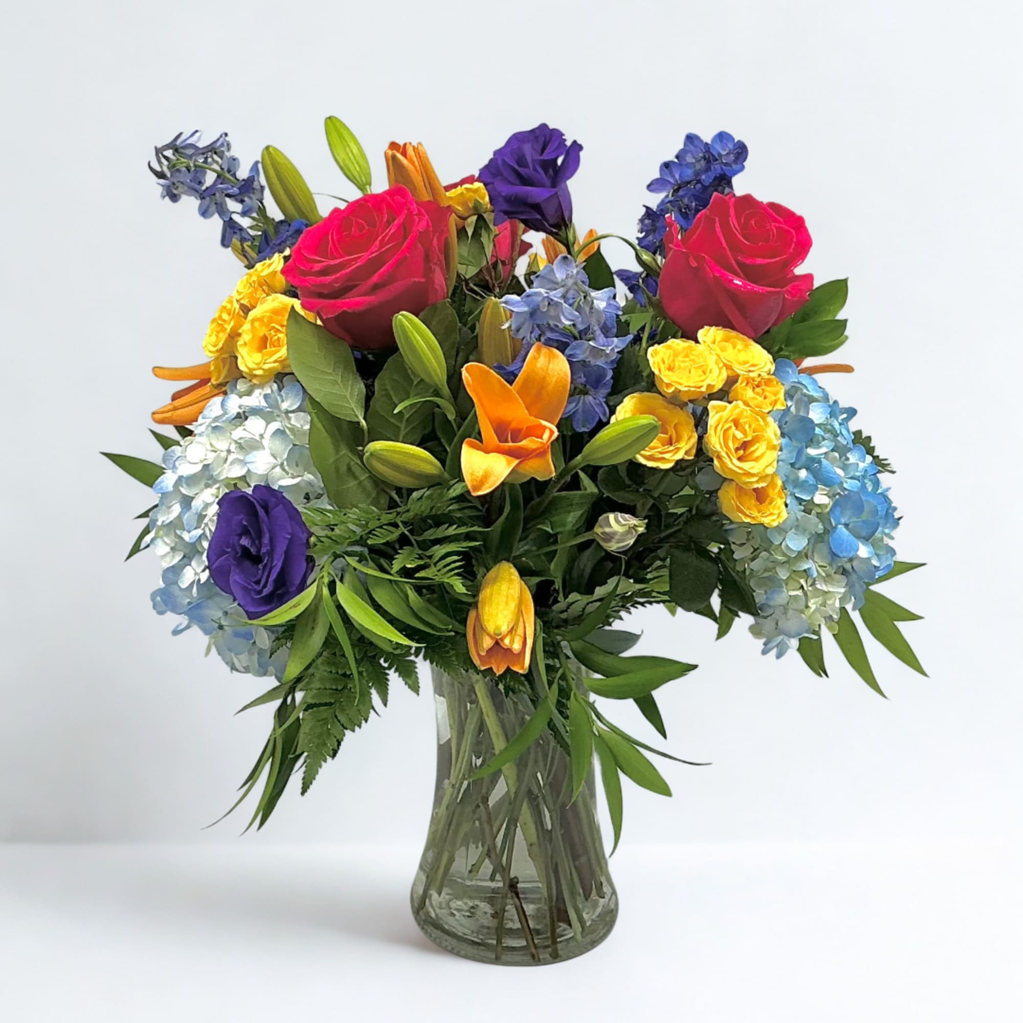 Colorful bouquet of roses, lilies, and hydrangeas in a clear glass vase